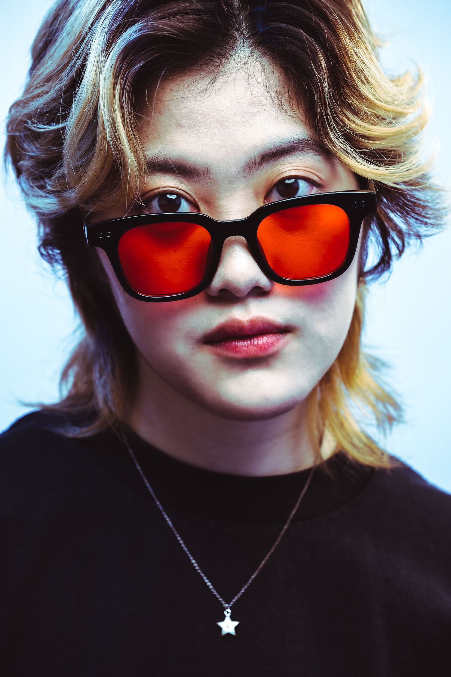 A series of portraits showing someone wearing red-tinted sunglasses and a black top with a small necklace pendant.