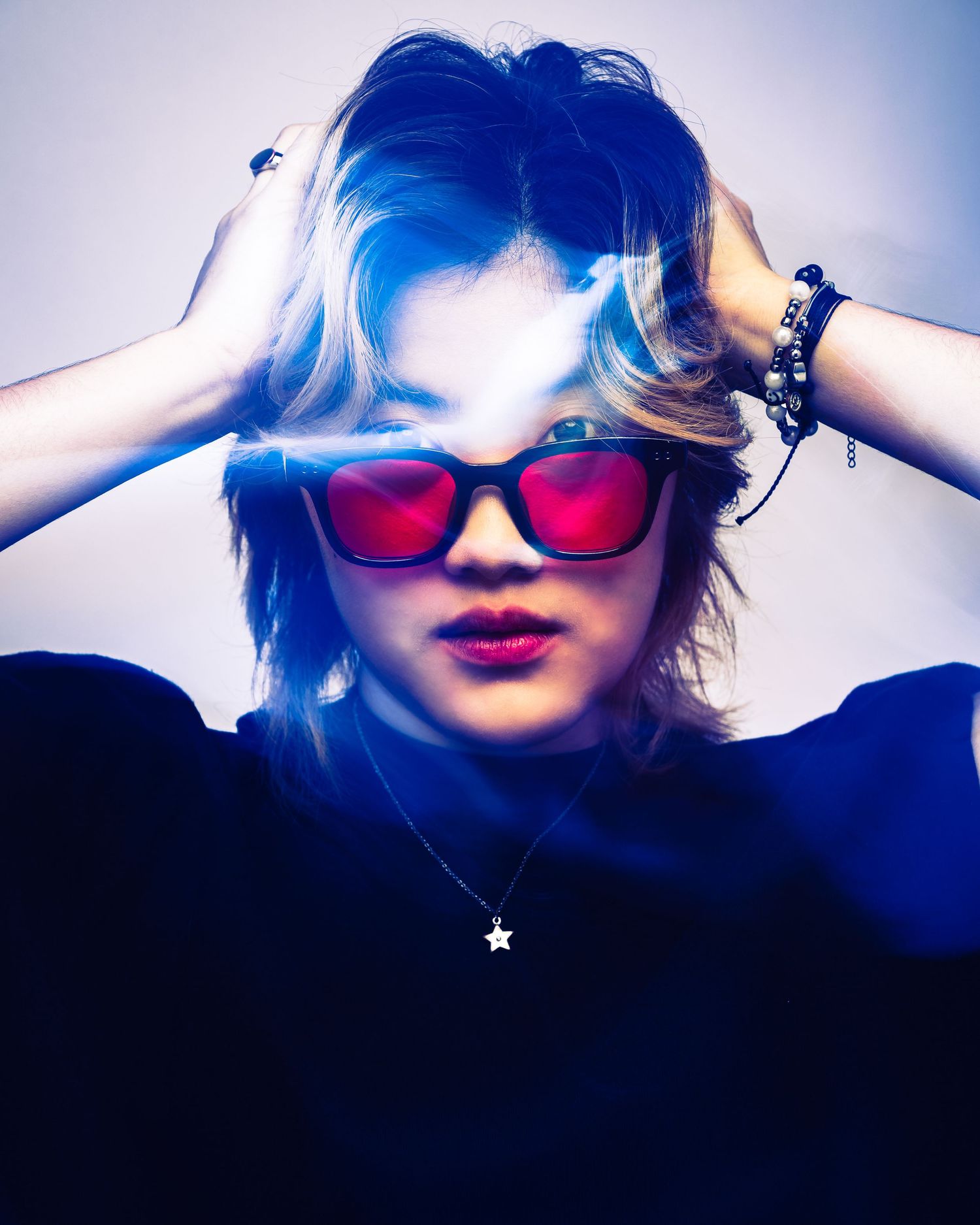 A person wearing red sunglasses poses in a creative blue-tinted photo series with dramatic lighting effects.