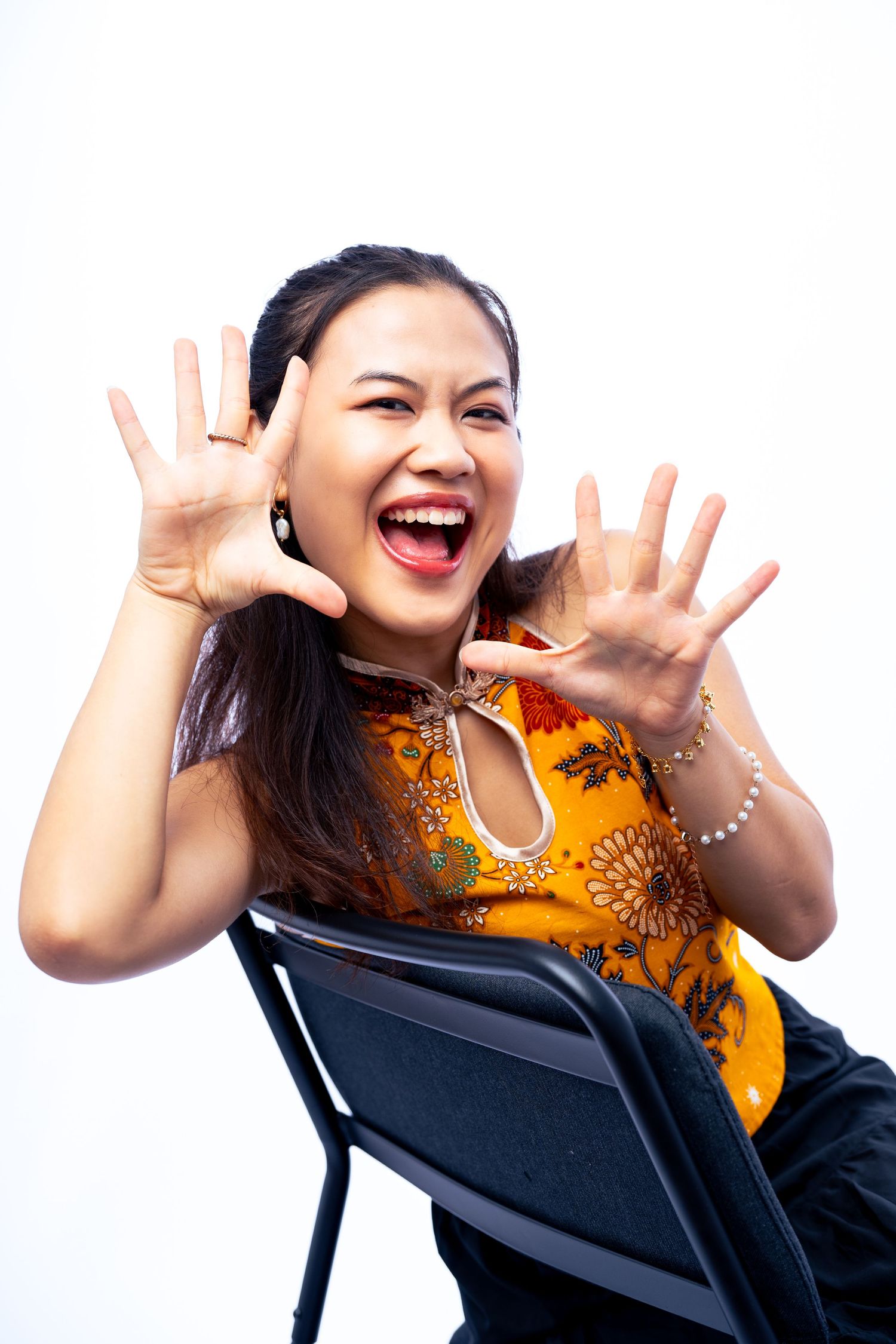 A person in an orange top sitting on a chair shows playful expressions and hand gestures in a photo series.