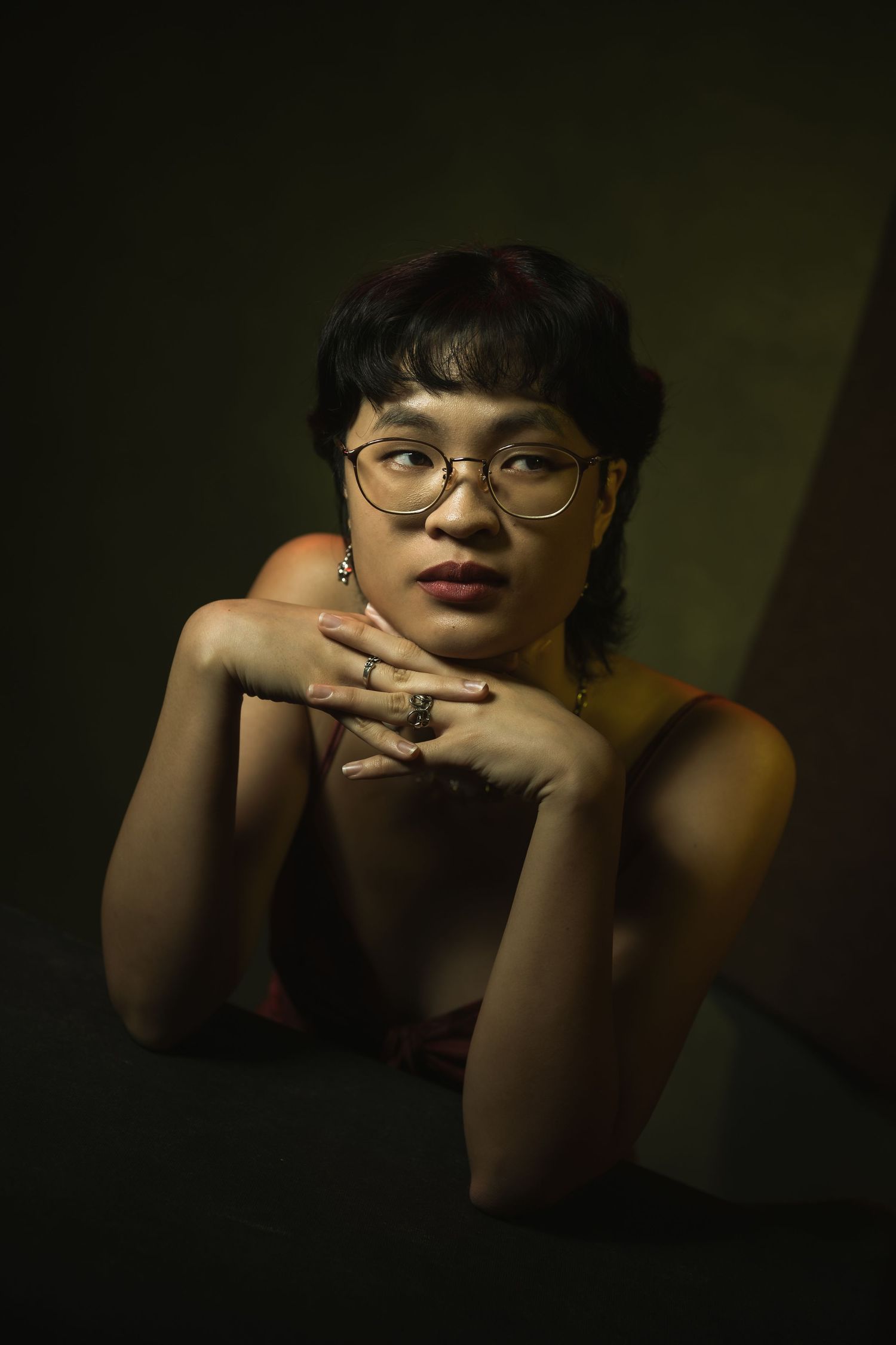 A moody portrait series showing someone in glasses resting their chin on their hands against a dark background.