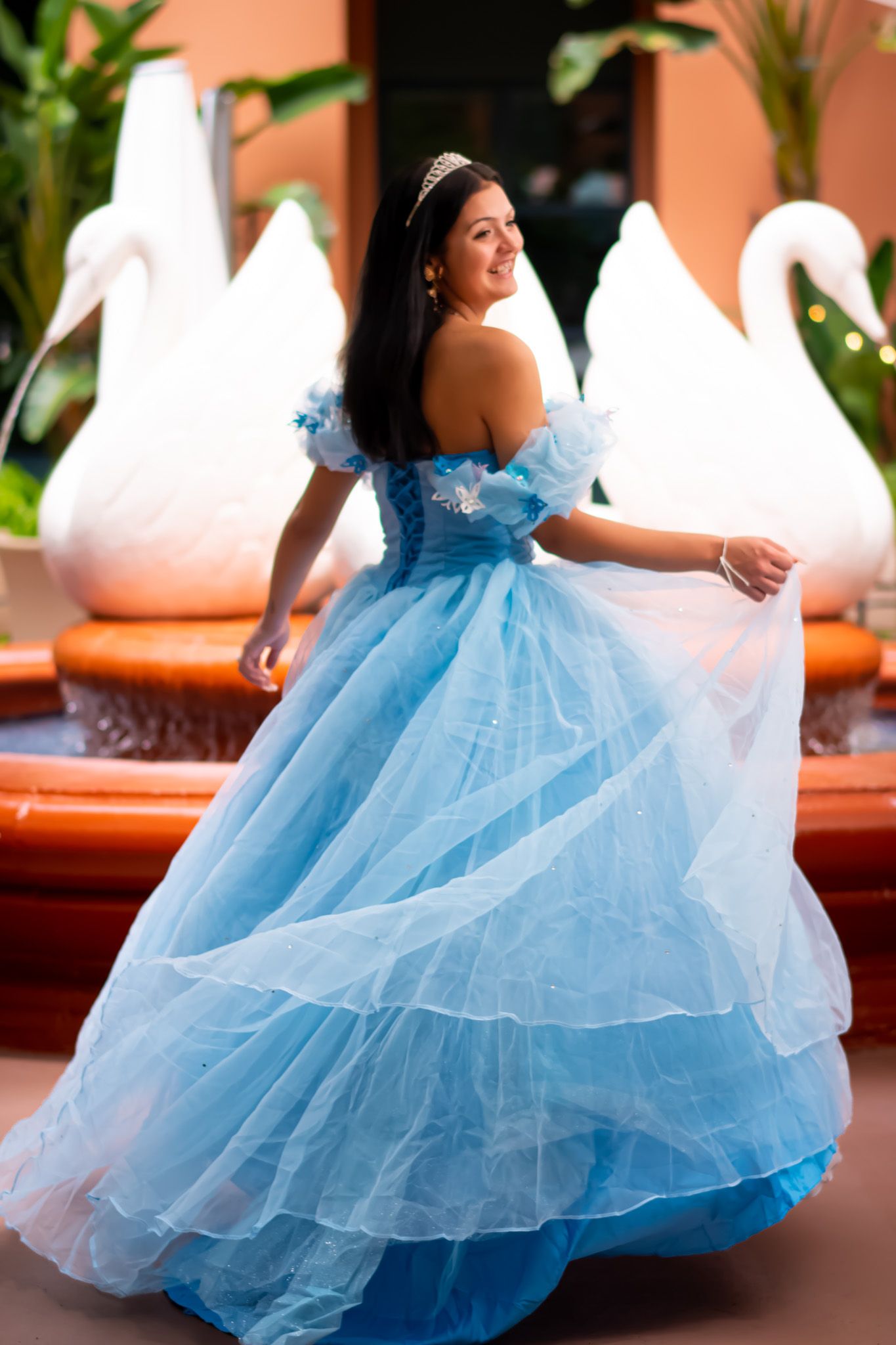 Woman in flowing blue princess ballgown twirls gracefully during a special occasion photoshoot.