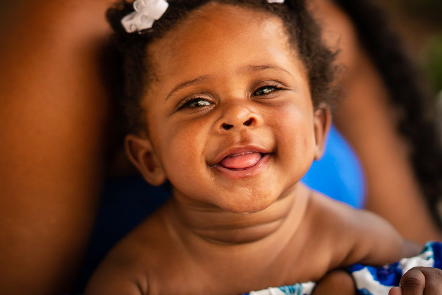 A joyful baby wearing a hair bow smiles brightly at the camera.