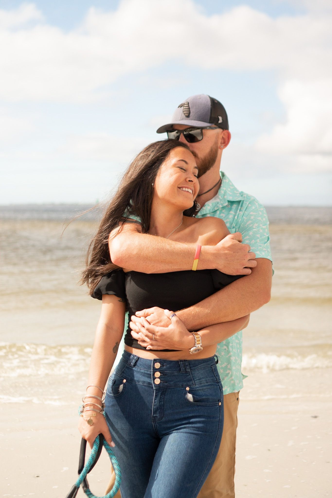 Couple embracing on sandy beach during sunset photoshoot.