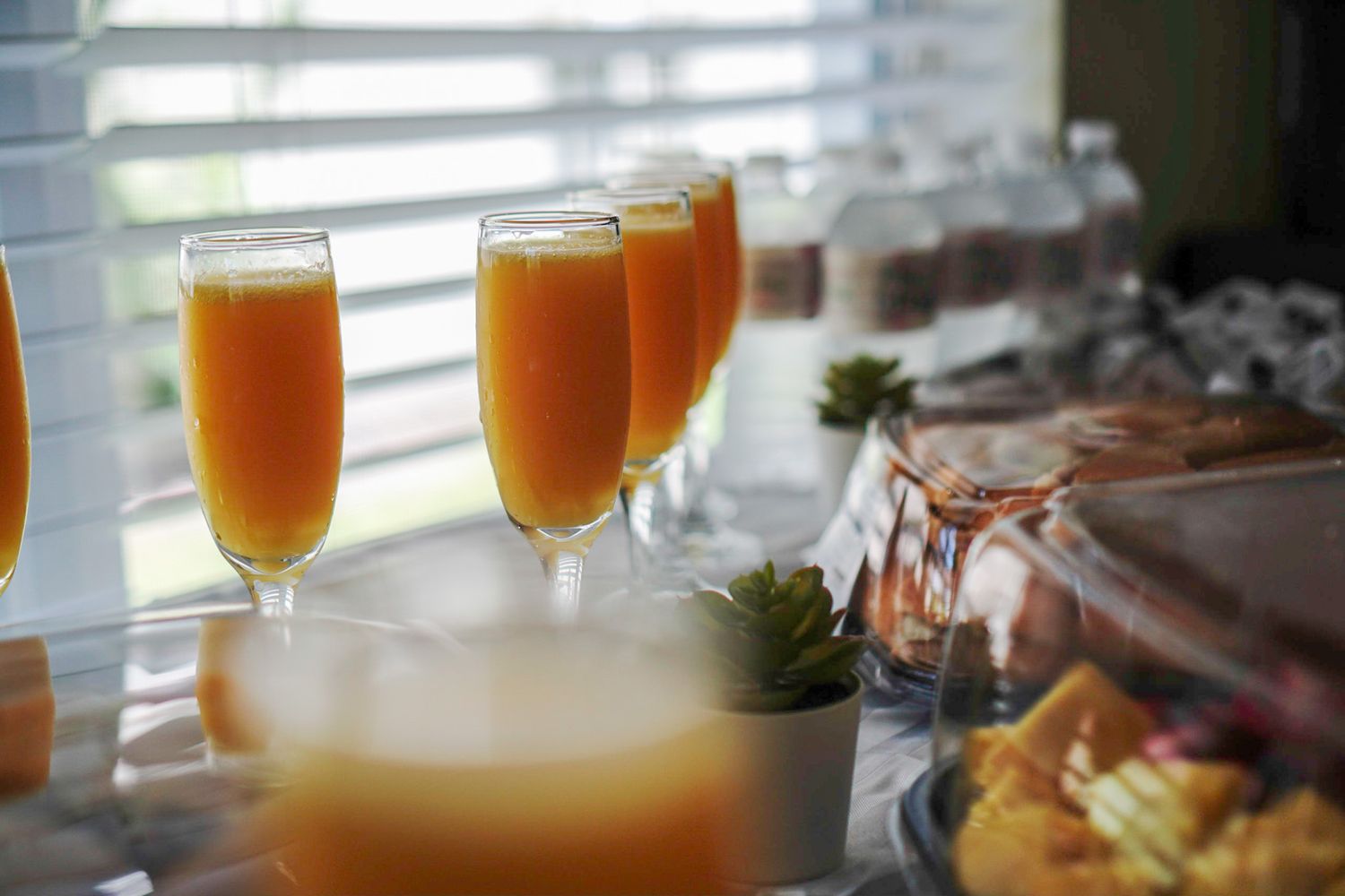 Orange mimosa cocktails lined up on a buffet table with window light streaming in.