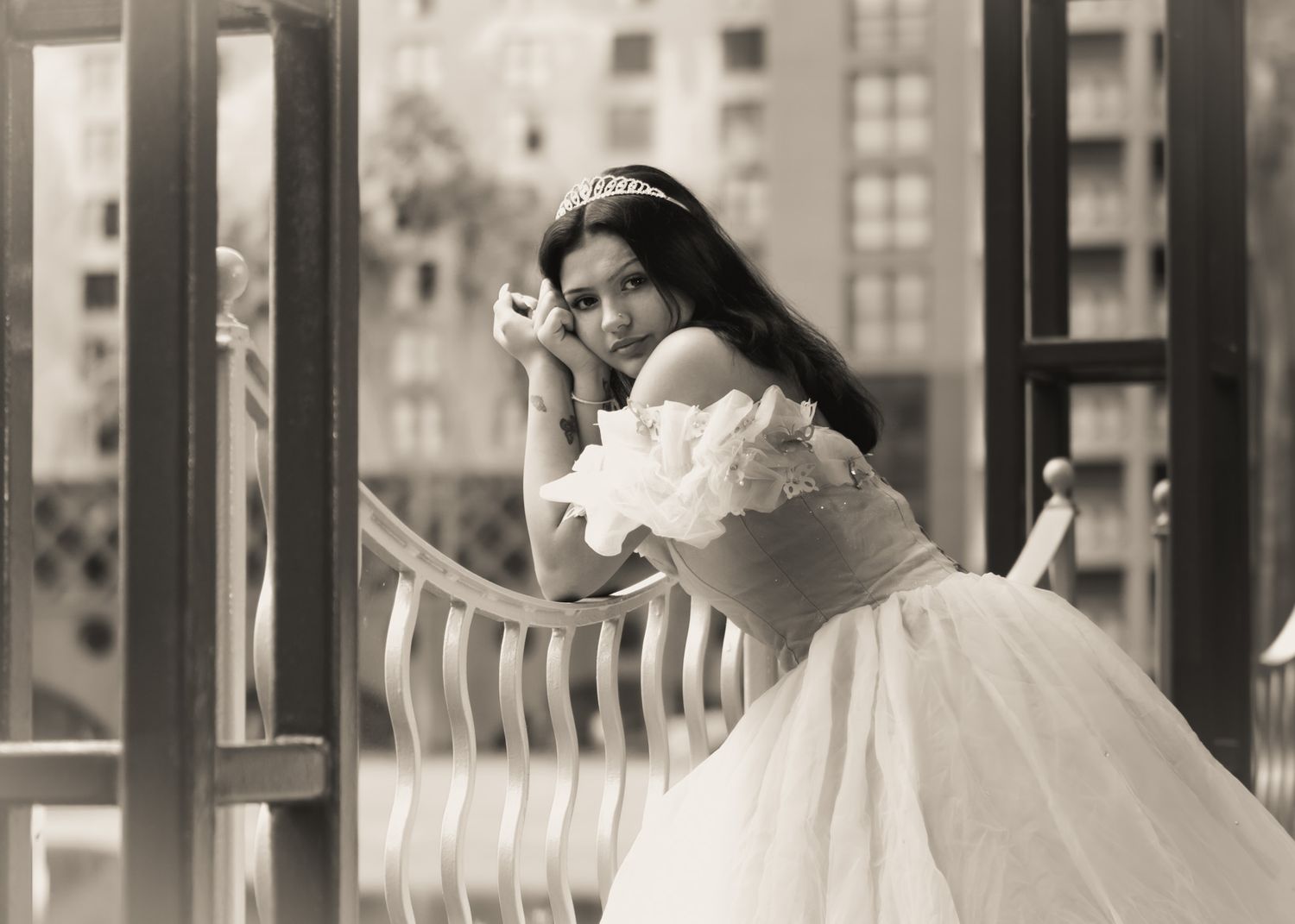 A woman in a vintage white dress poses elegantly on a balcony in black and white.