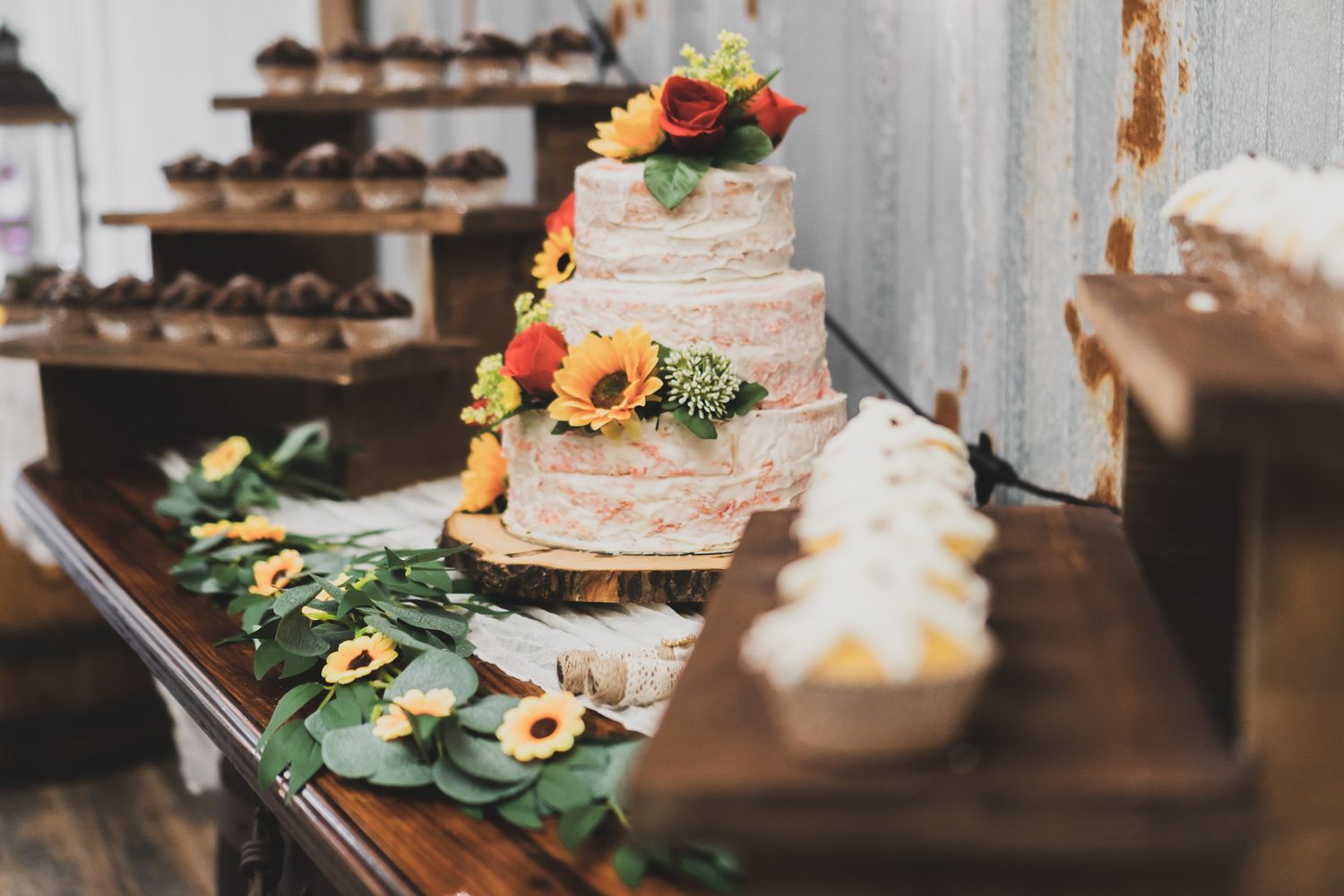 Rustic wedding cake display with sunflowers and greenery decorations.
