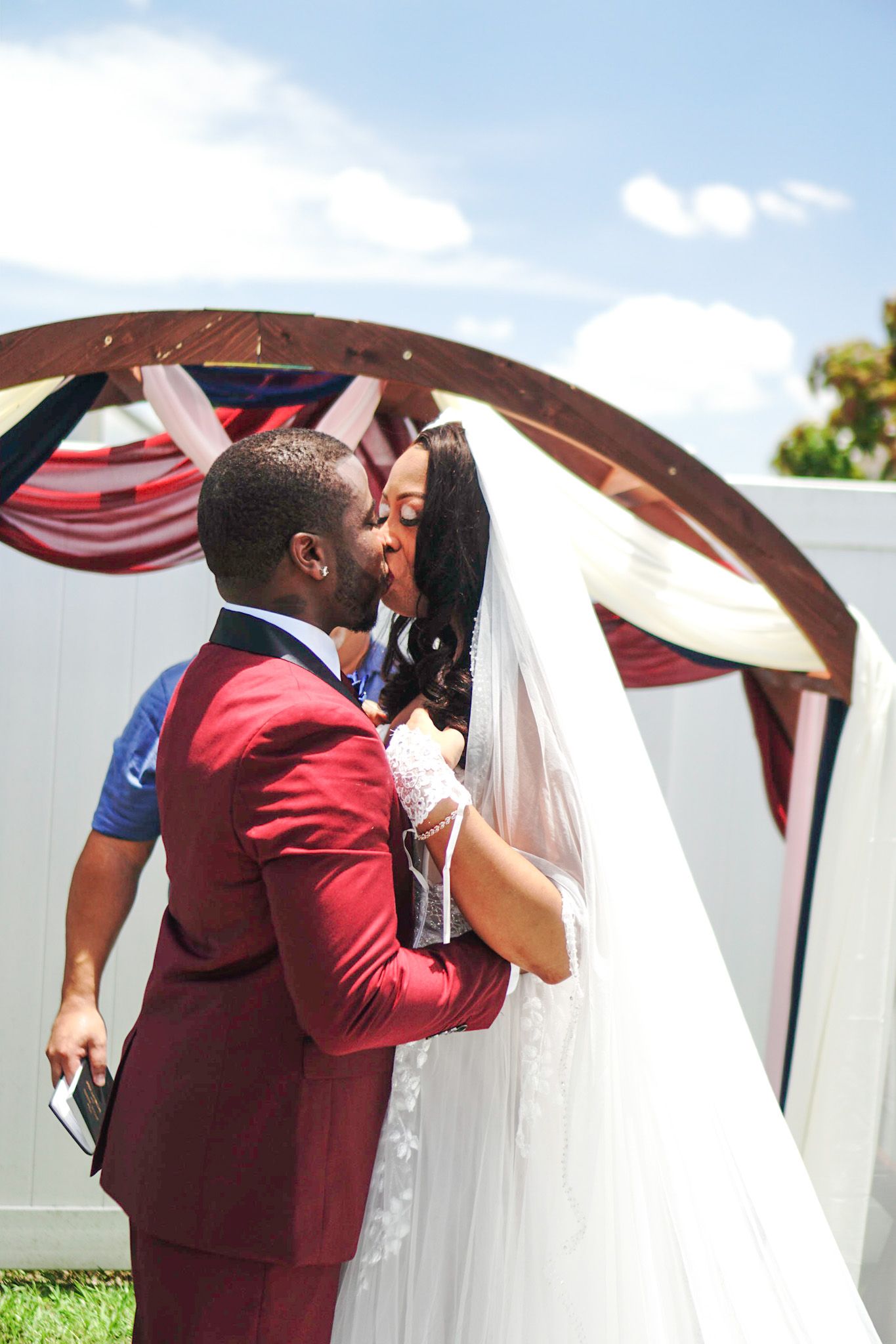 Romantic wedding moment captured outdoors against a white wall and blue sky.