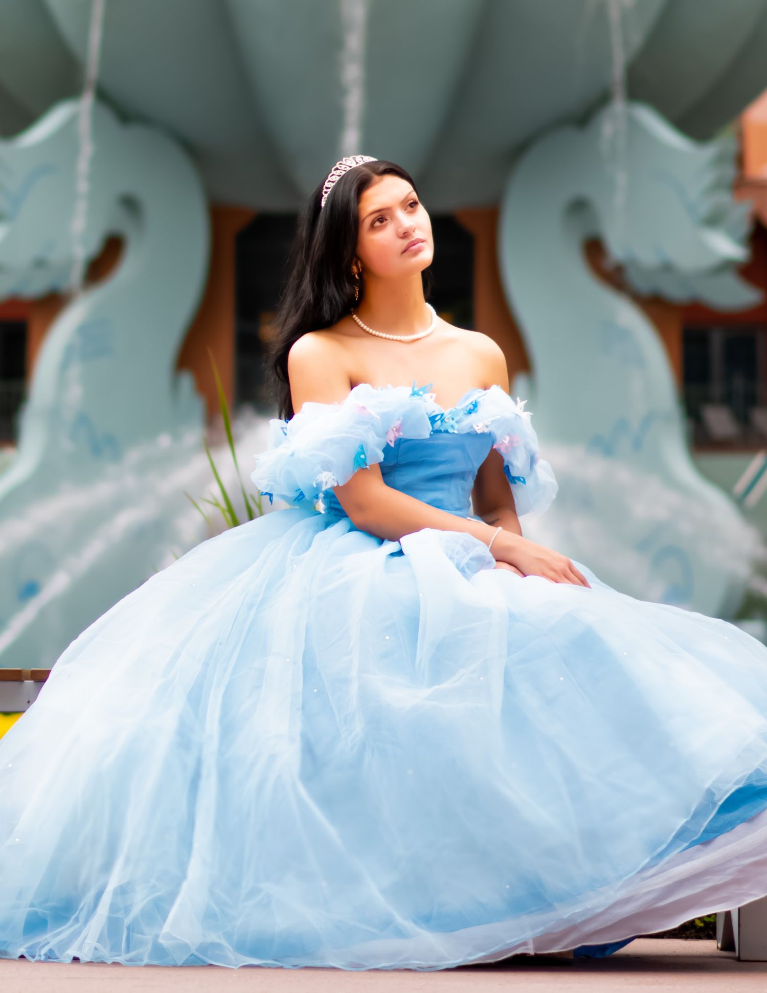 A model in a light blue princess ball gown poses outdoors against a decorative backdrop.
