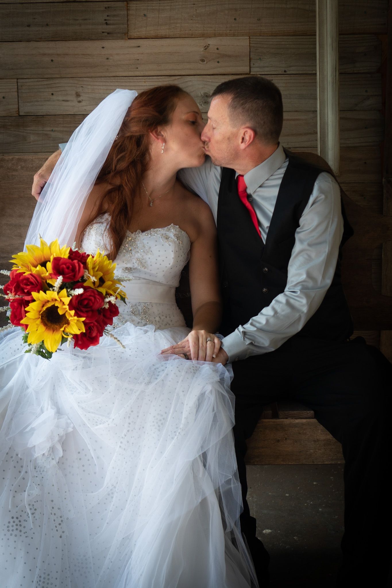 Wedding couple sharing intimate moment with sunflower bouquet in rustic wooden setting.