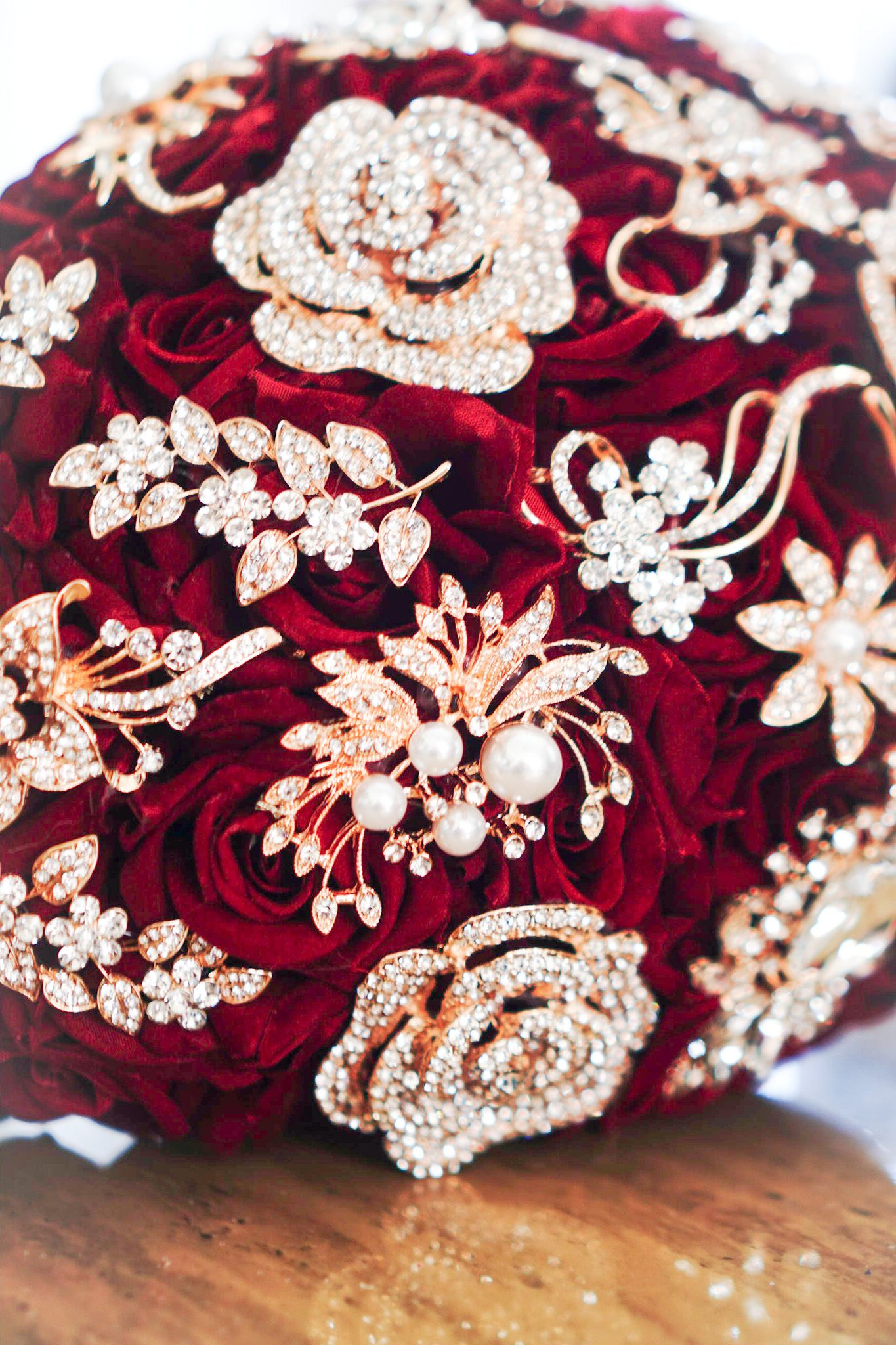 A stunning bridal bouquet featuring deep red roses adorned with crystal brooches and pearl decorations.