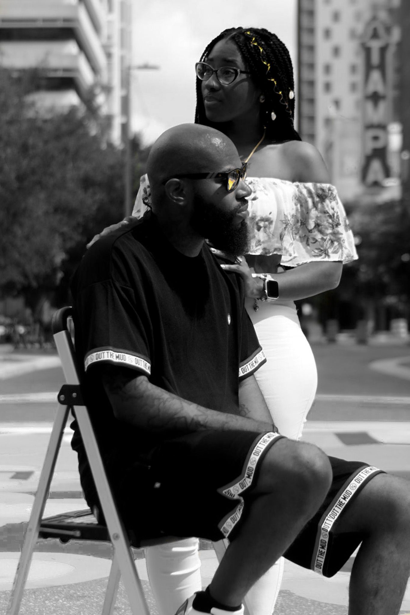 Person in black attire sitting outdoors in an urban setting during a photo session.