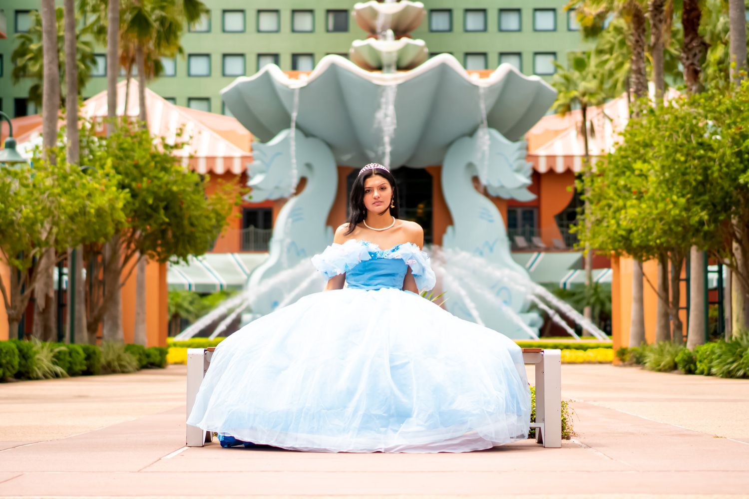 A woman in a blue ball gown poses in front of a decorative outdoor fountain.