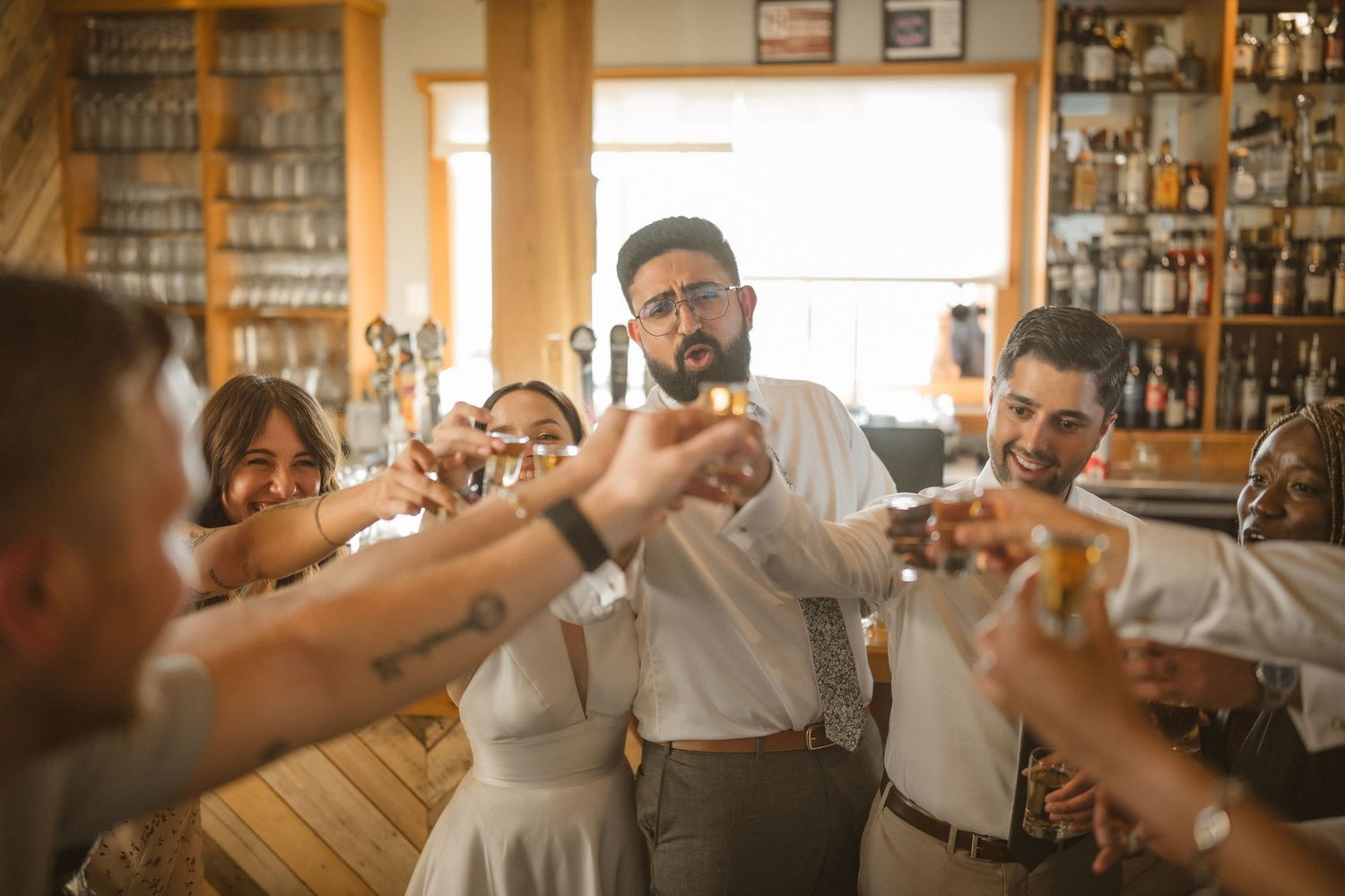 A group of people toast together with drinks at a rustic bar, creating a warm celebratory atmosphere.