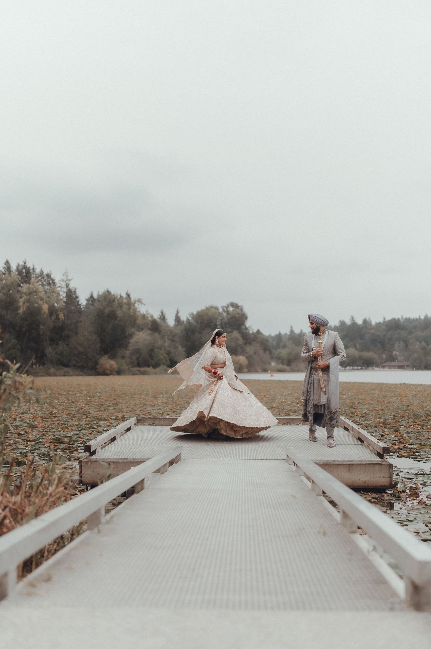 A couple in formal attire posing on a wooden dock by a misty lake.