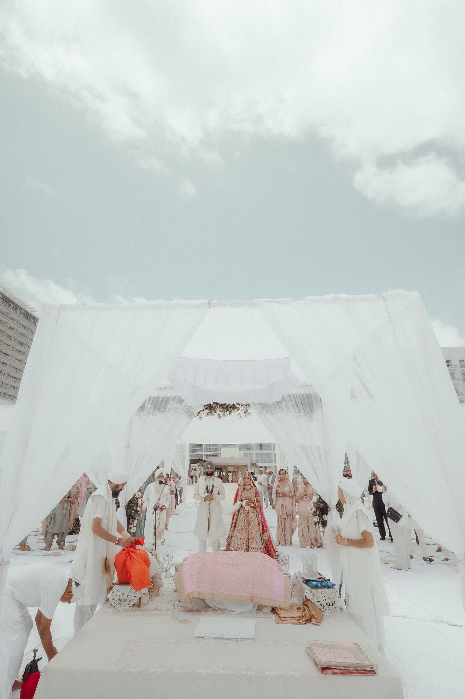 An outdoor wedding ceremony setup with white flowing fabric canopy and pink and white decor under a cloudy sky.