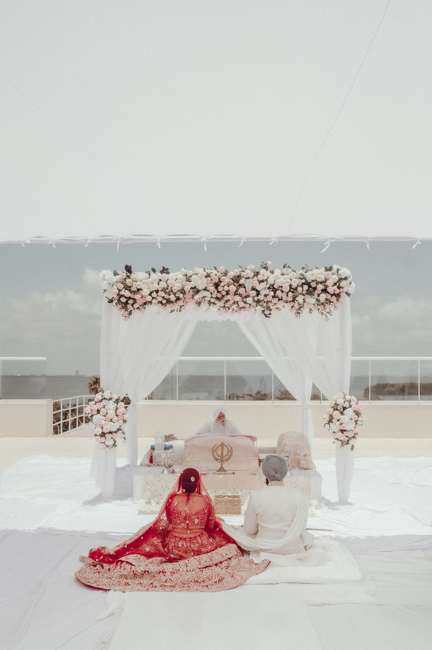 Luxurious beachfront Sikh wedding ceremony setup with white mandap and floral arrangements on a pristine sandy shore.