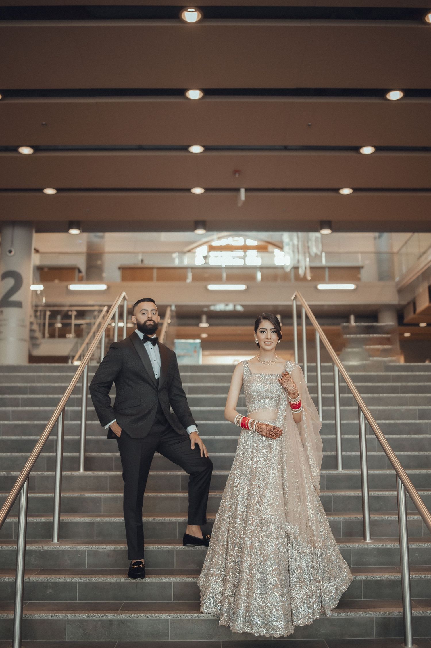 A couple poses playfully on gray concrete steps in an indoor setting with modern lighting.