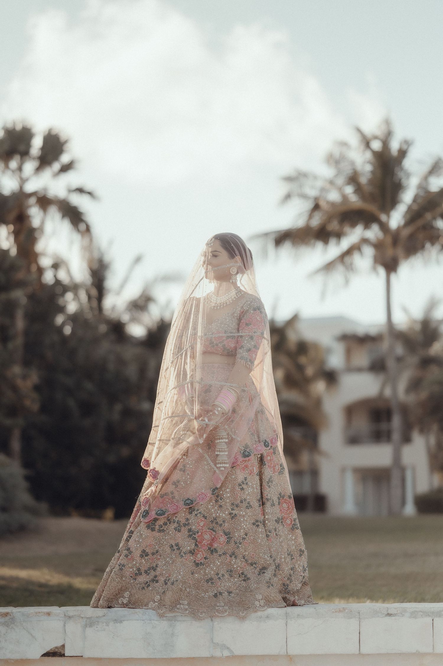 A delicate floral dress photographed against a backdrop of palm trees and white buildings in soft lighting.