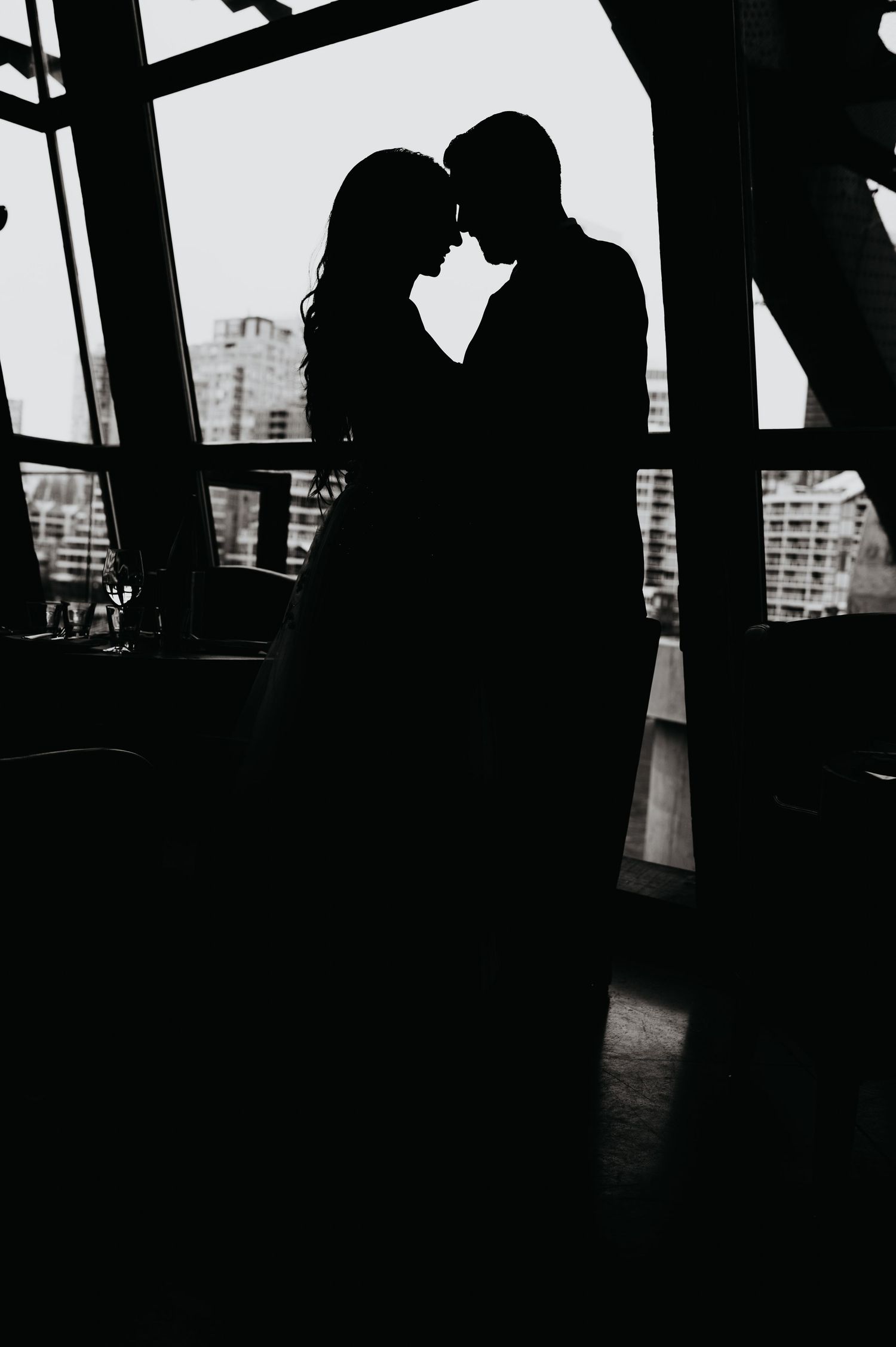 Four silhouettes of people in dramatic lighting at a high-rise looking out large windows over a city skyline.