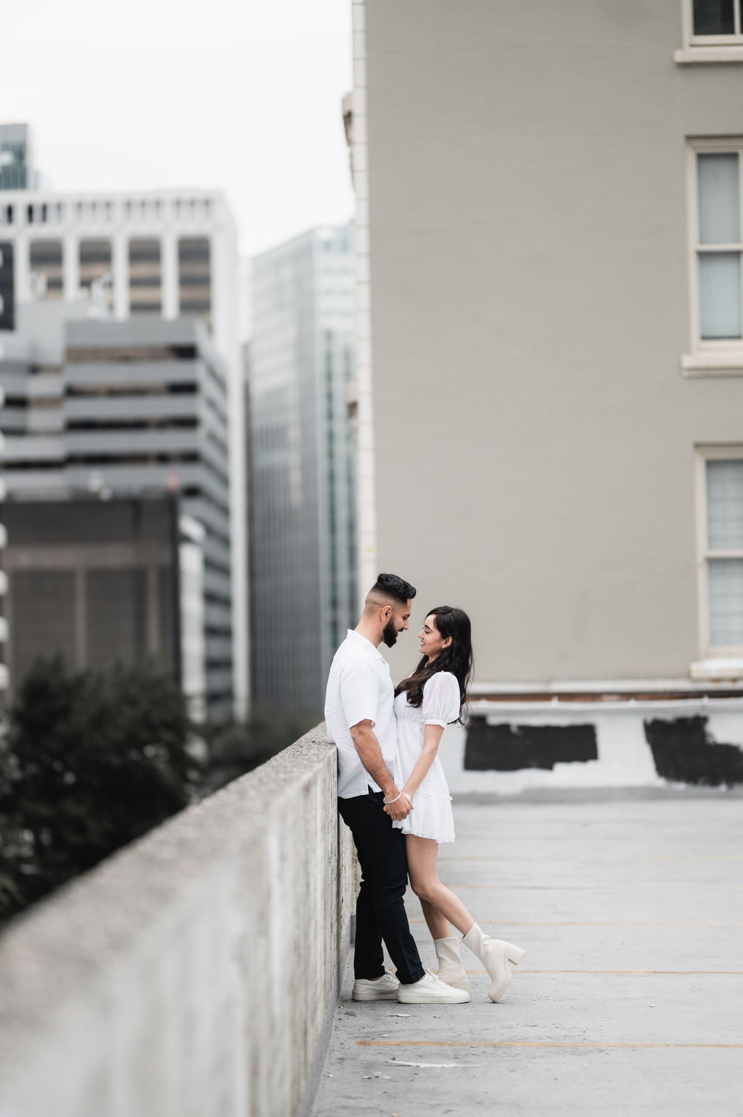 Couple sharing intimate moment on urban rooftop with city buildings in background.