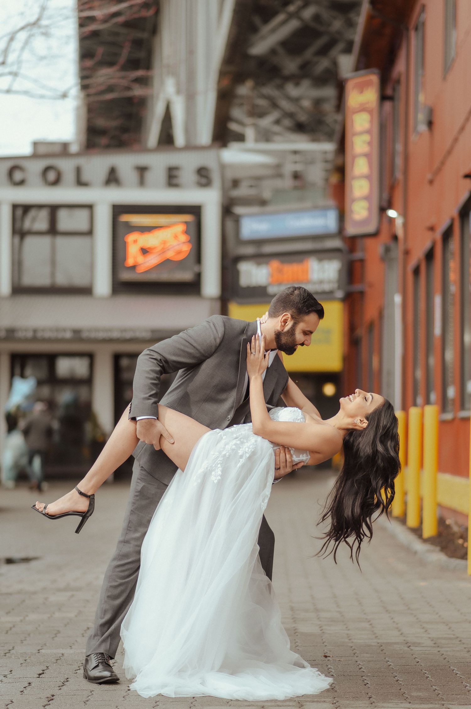 A dramatic dip kiss photographed in front of urban storefronts and brick buildings.