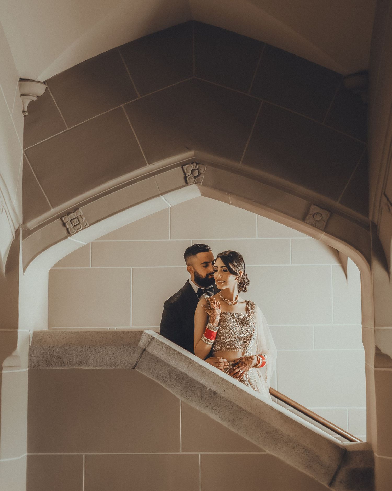 A couple shares an intimate moment together in an architectural stairwell with dramatic lighting.