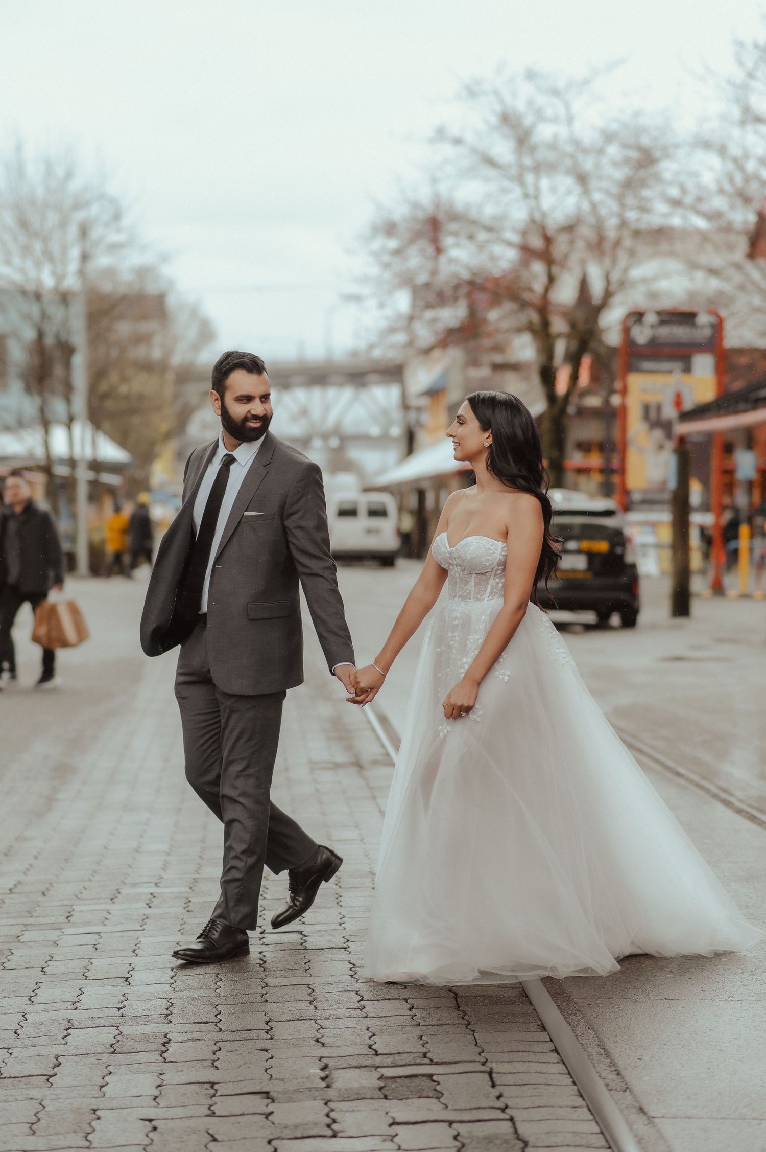 A playful couple holds hands while walking on cobblestone streets in wedding attire.