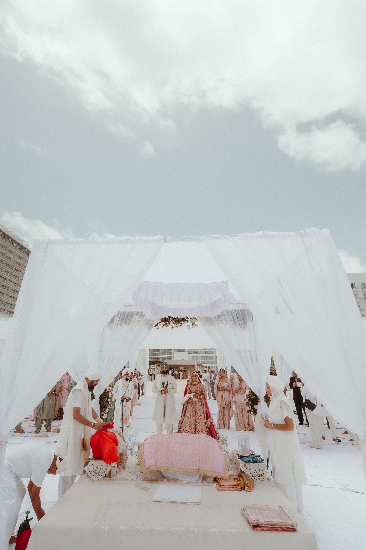 White wedding tent setup on a beach with chairs and decorations under cloudy skies.