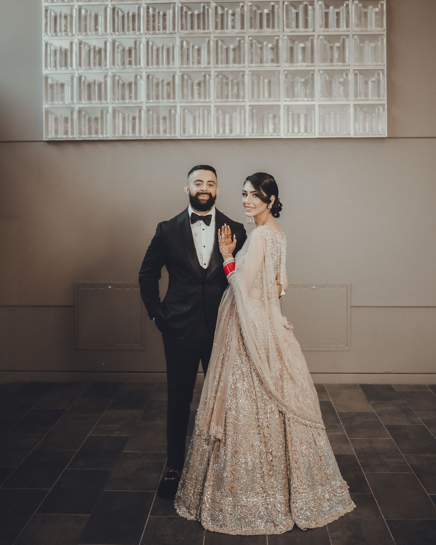 A couple in a traditional wedding attire poses against a modern architectural wall with geometric patterns.