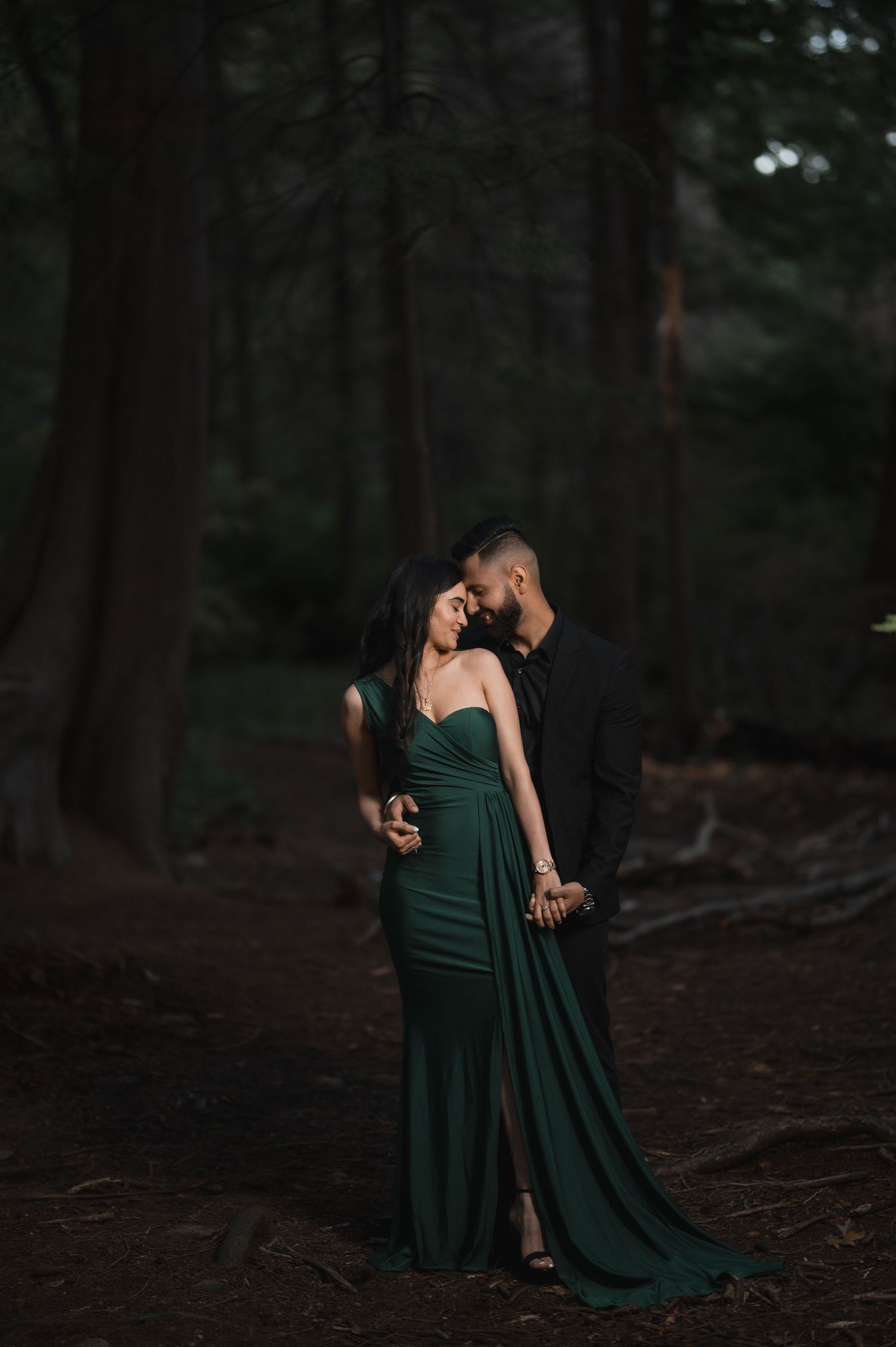Couple in elegant attire sharing an intimate dance in a wooded area.