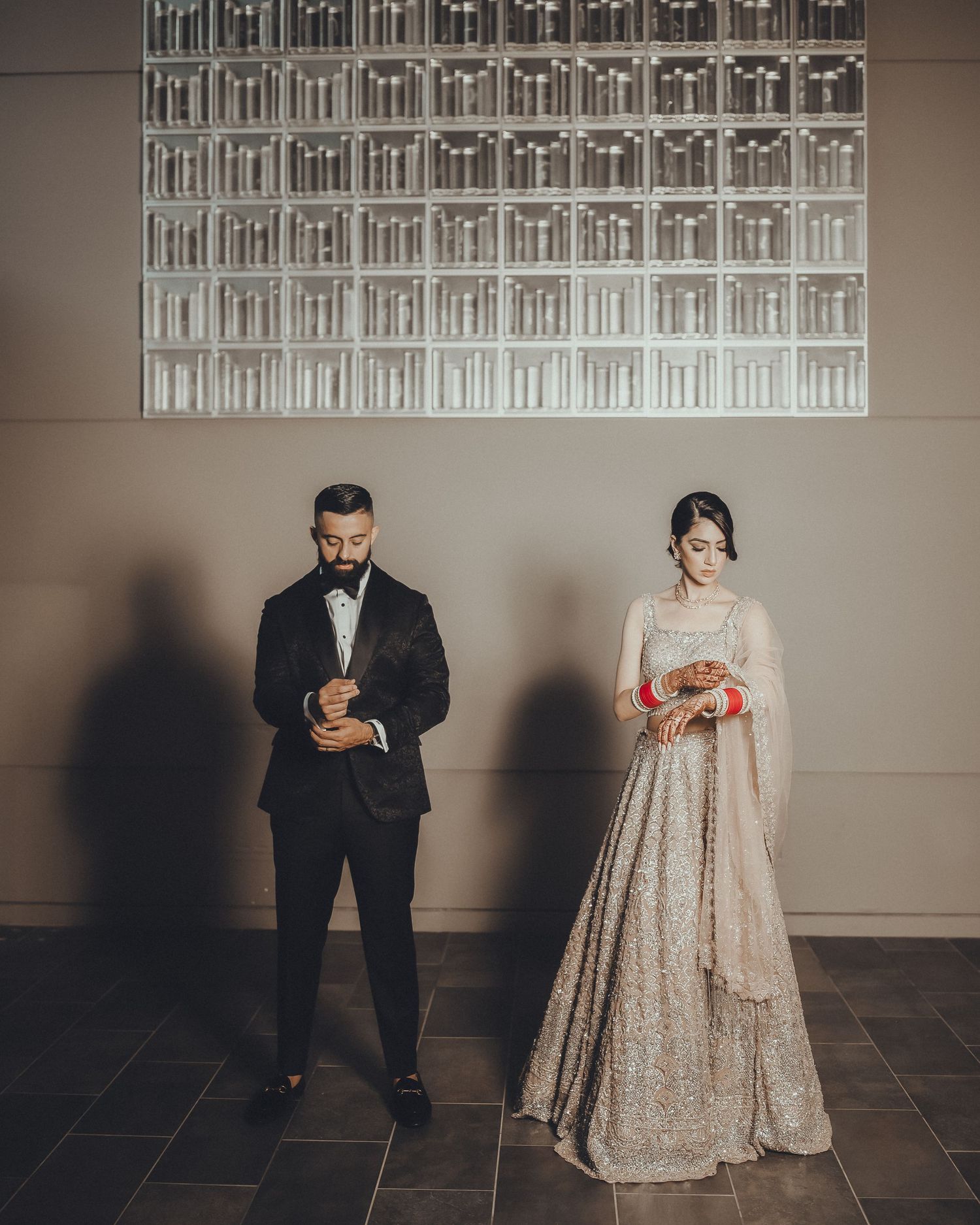 A couple in wedding attire stands in a modern gallery space with geometric lighting patterns on the wall.