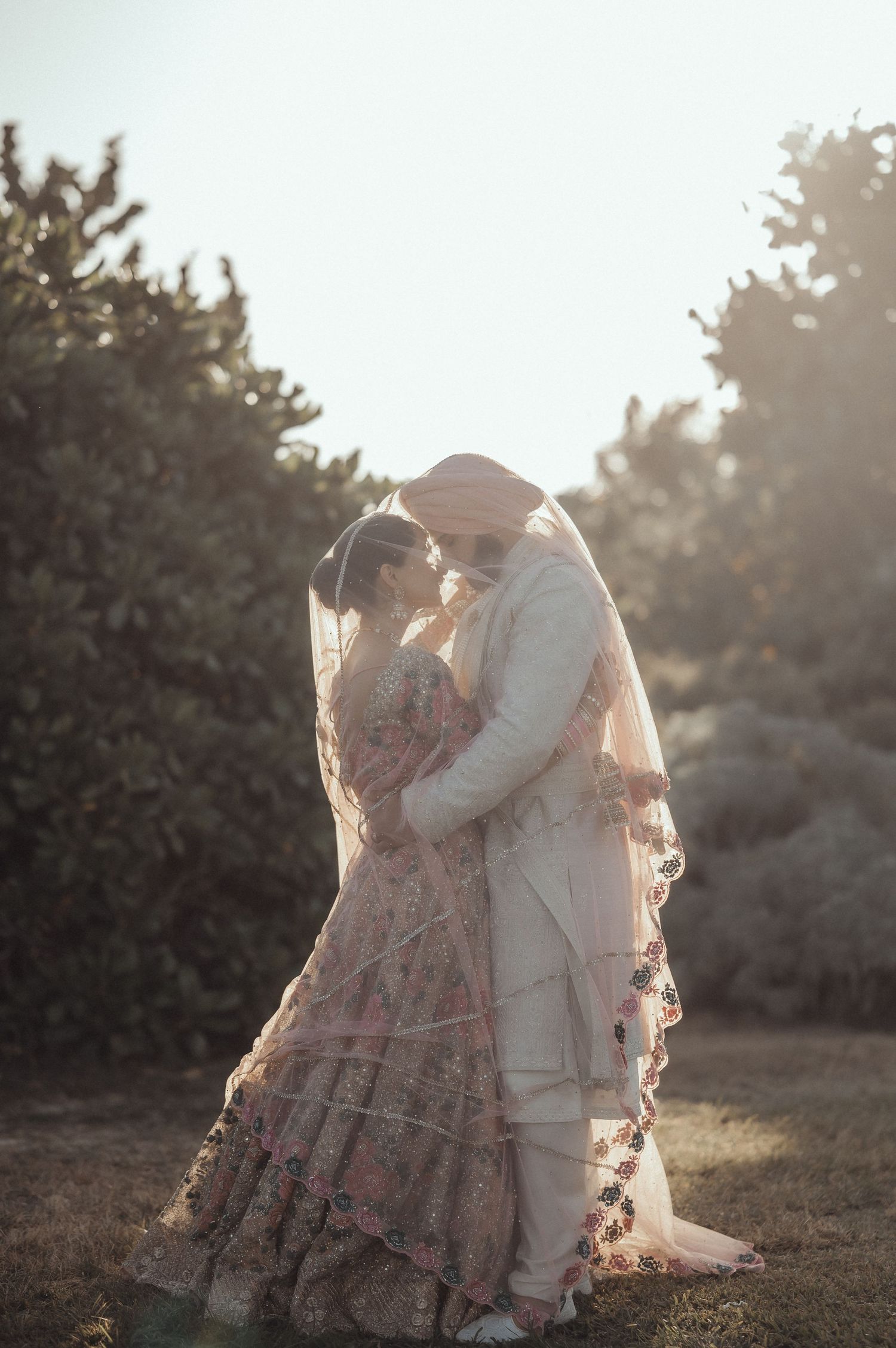 Two people in flowing dresses dance together in a sunlit field during golden hour, creating a dreamy ethereal scene.