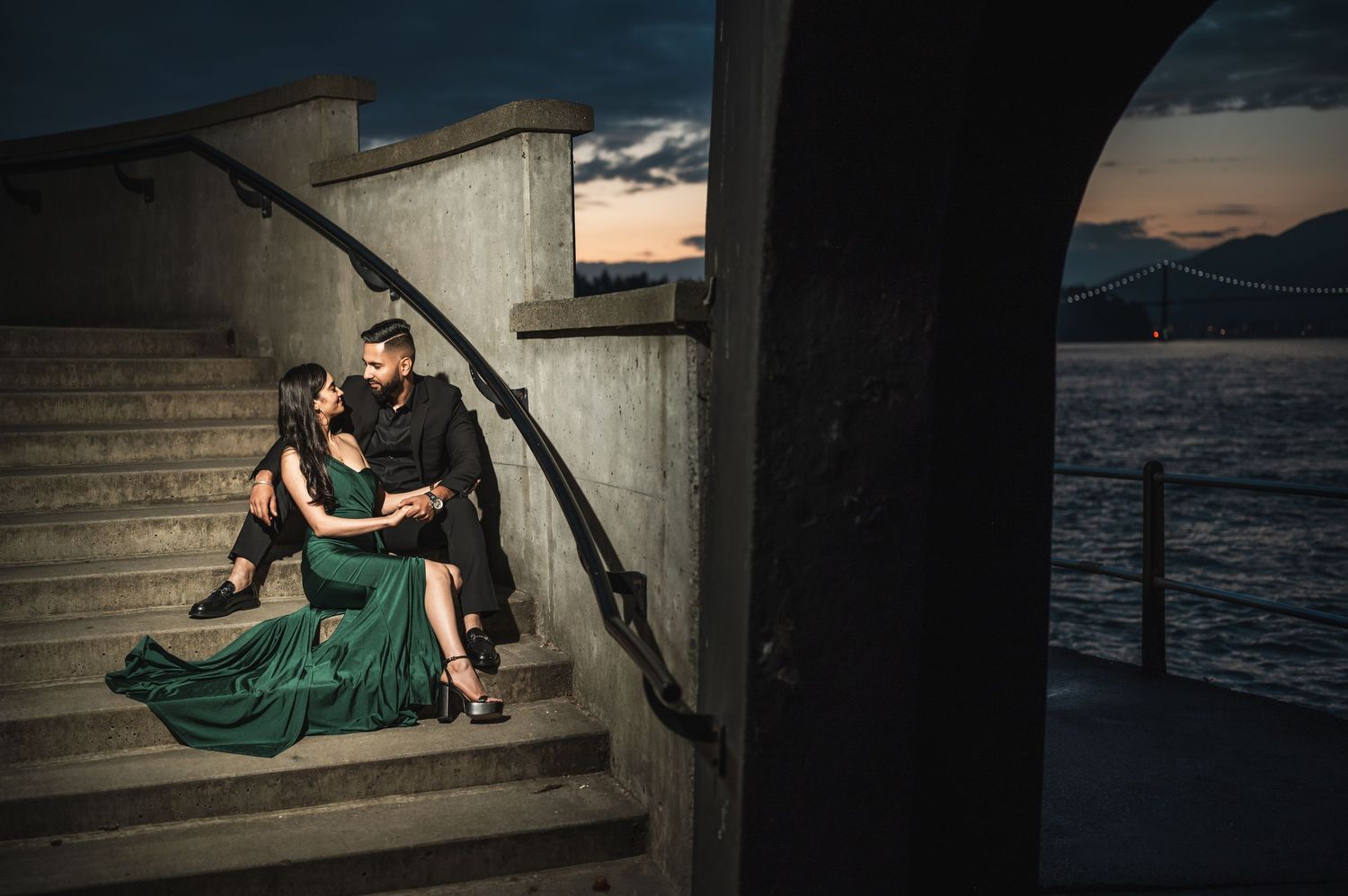 Romantic couple reclining on concrete steps with waterfront view at twilight.