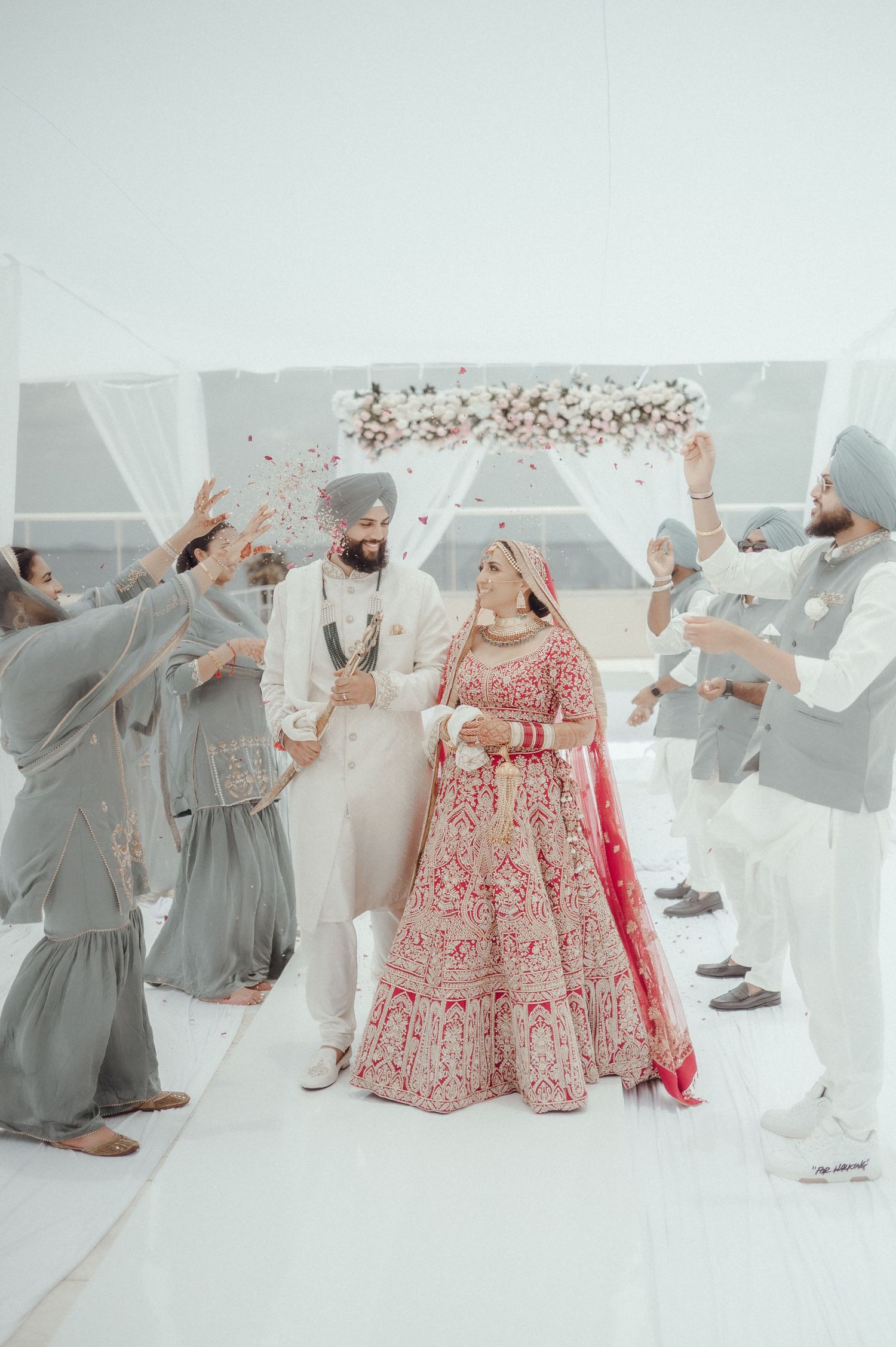 Bridesmaids in gray dresses throw their veils in celebration while bride poses in traditional red lehenga.