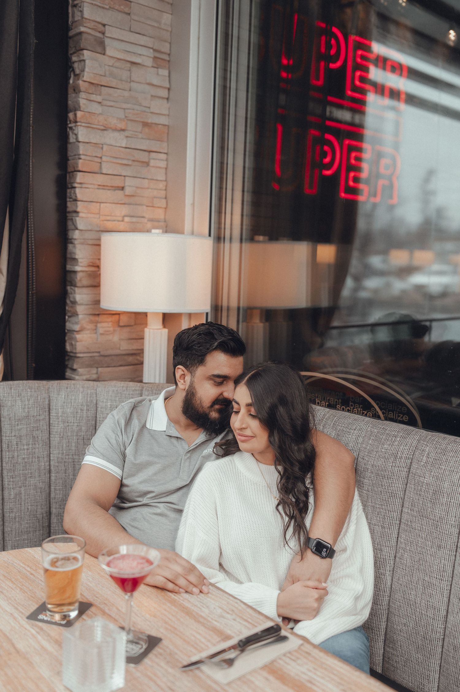 Couple looking at menu while seated in restaurant booth beneath neon signage.