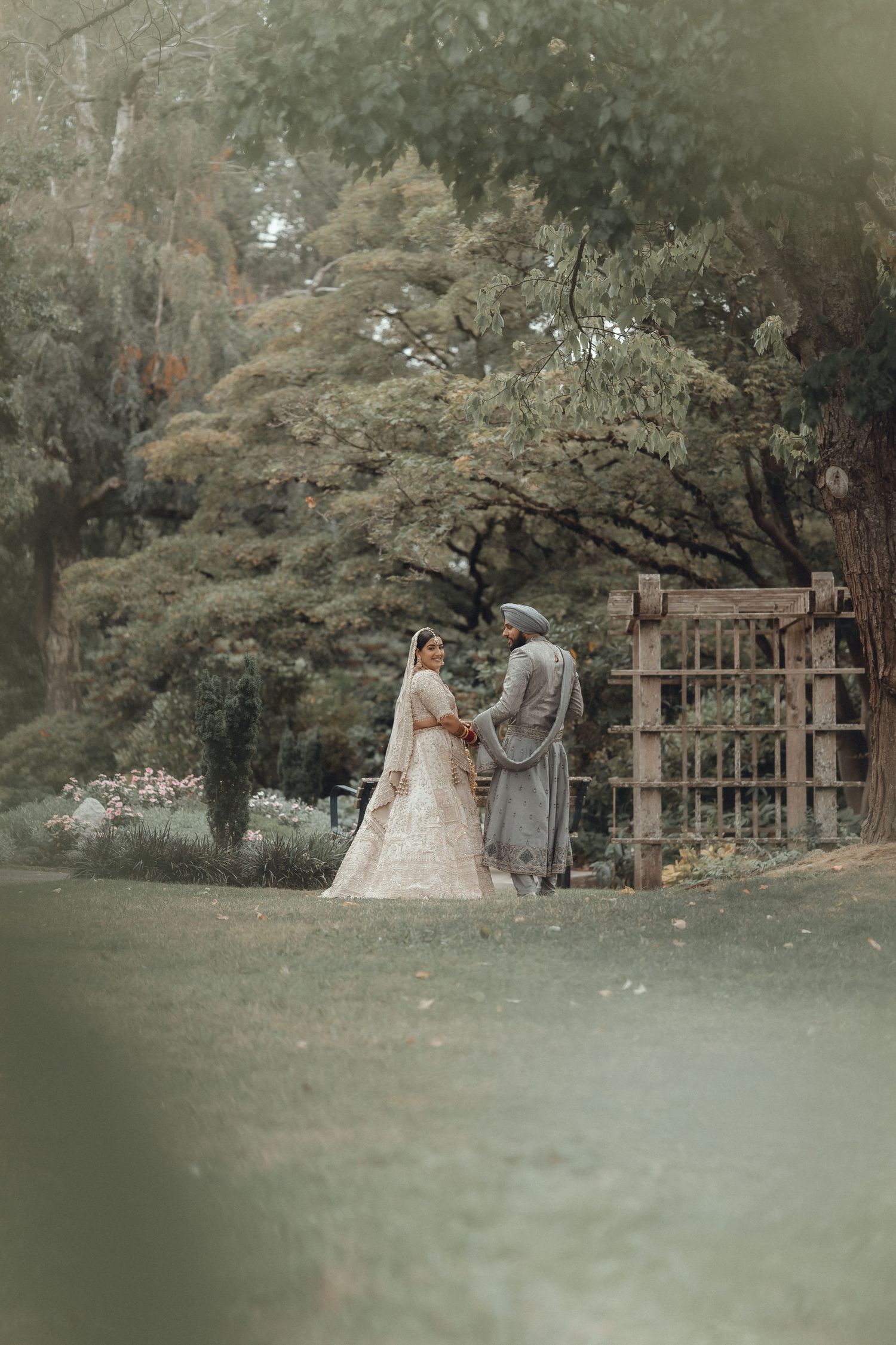 A couple in elegant traditional outfits standing together in a serene garden setting.