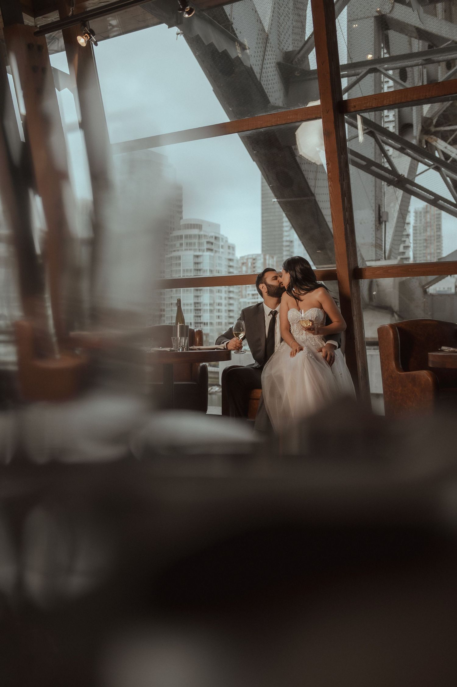 A romantic couple shares an intimate moment on a modern rooftop venue with urban architecture visible in the background.