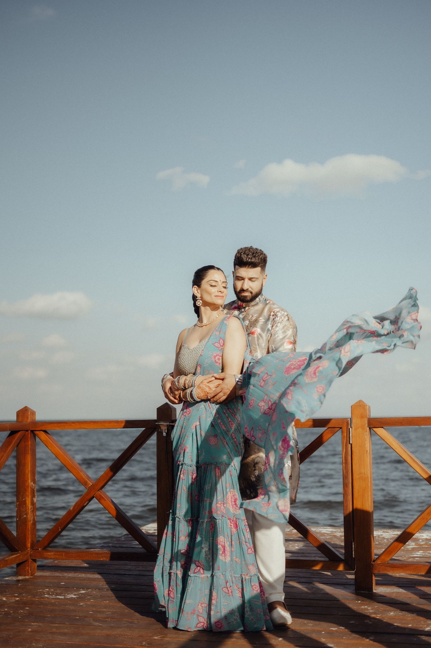 Couple in matching outfits dancing together on a wooden pier by the ocean during sunset.