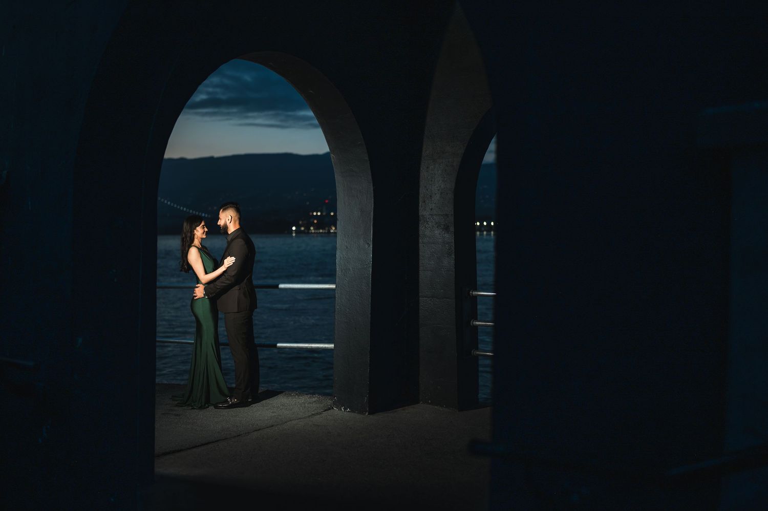 Couple sharing romantic moment under seaside arches at dusk.