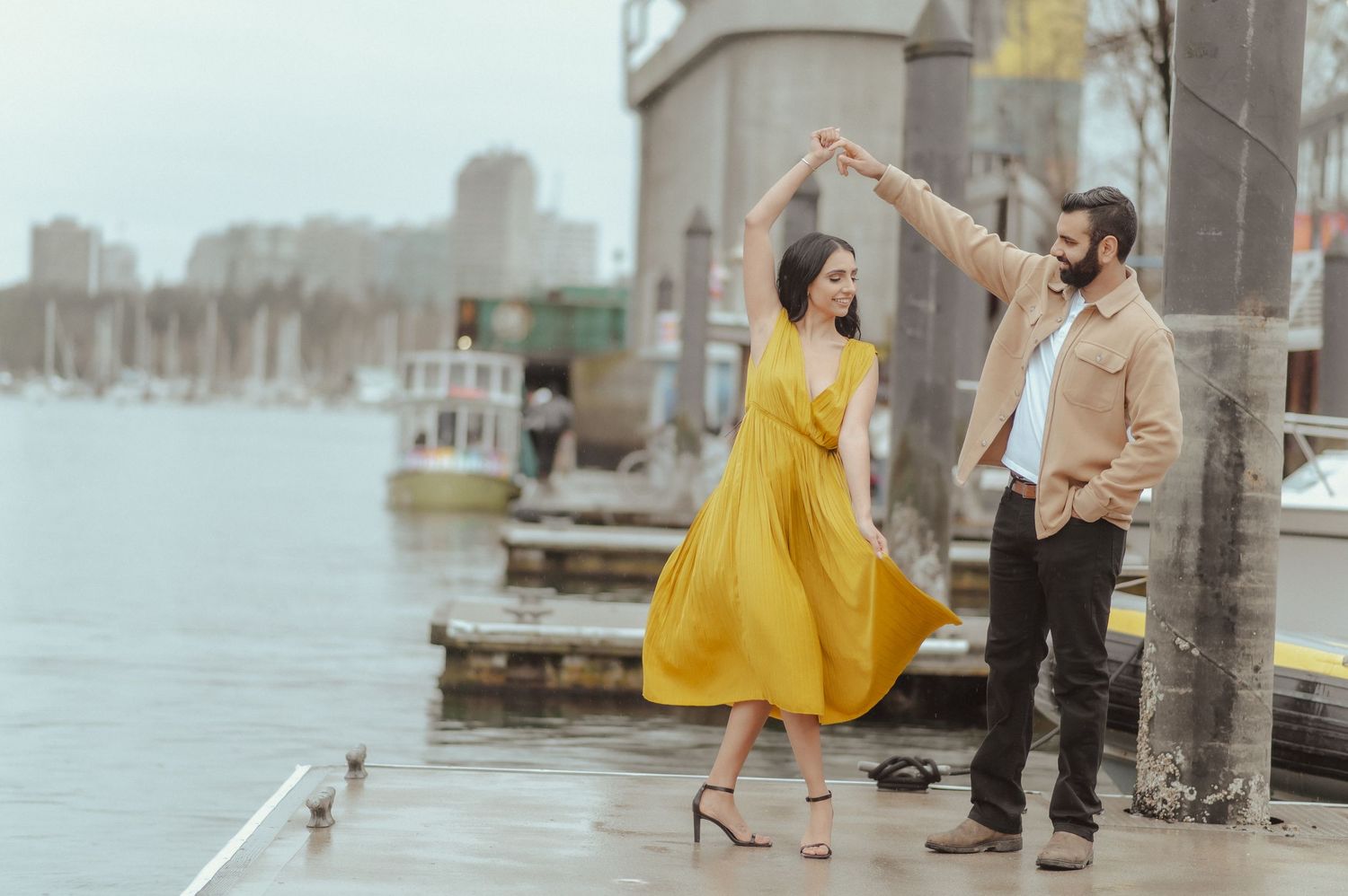 A couple dancing and twirling in a romantic moment by a harbor.