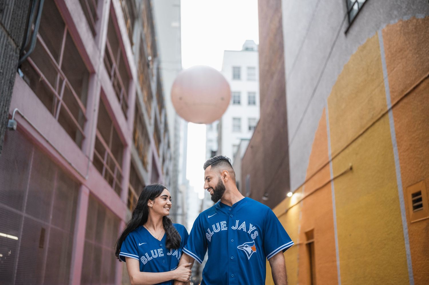 Couple playing with balloons in colorful urban alleyway.