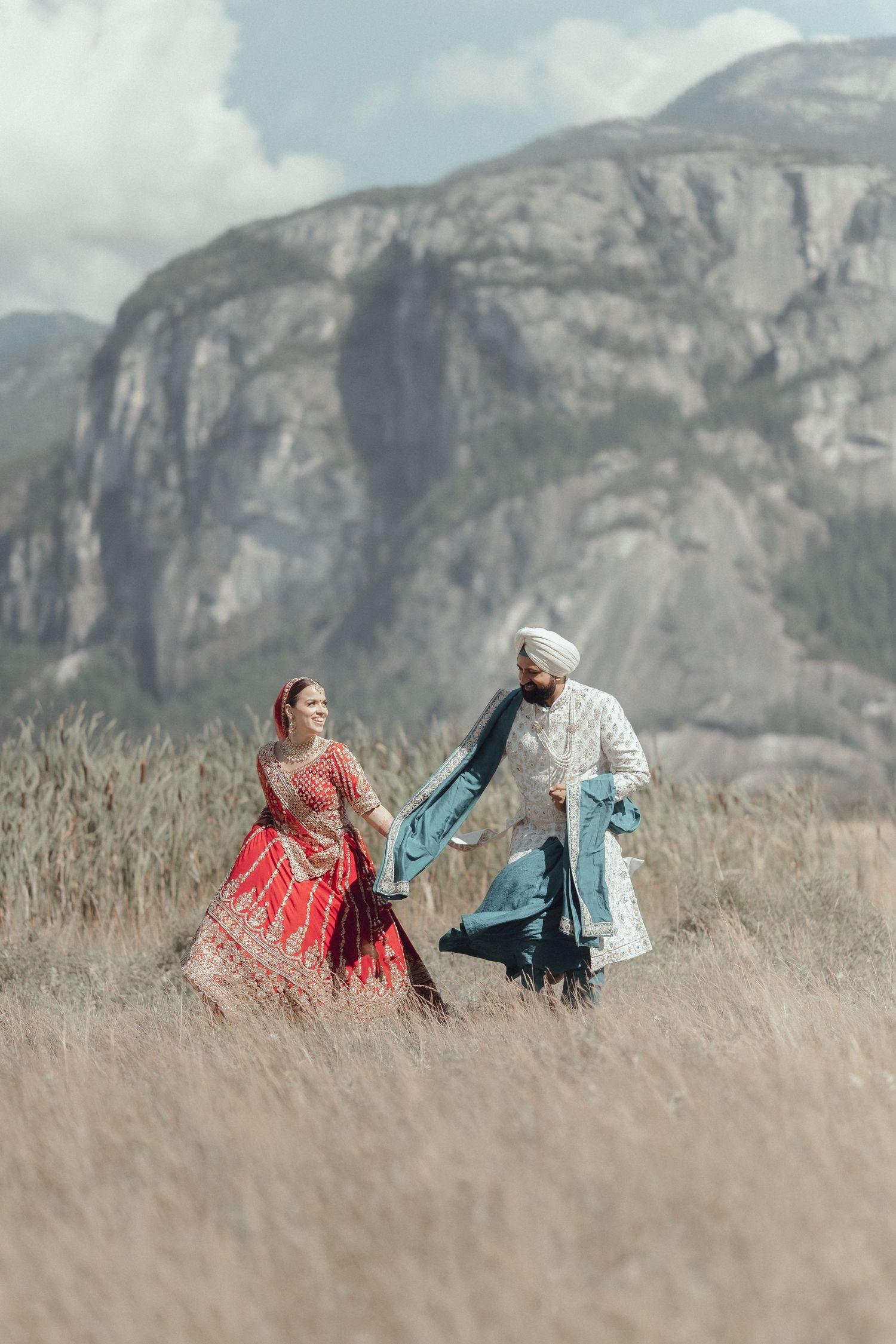 Two figures in vintage attire dance romantically in a meadow with dramatic mountain cliffs as their backdrop.