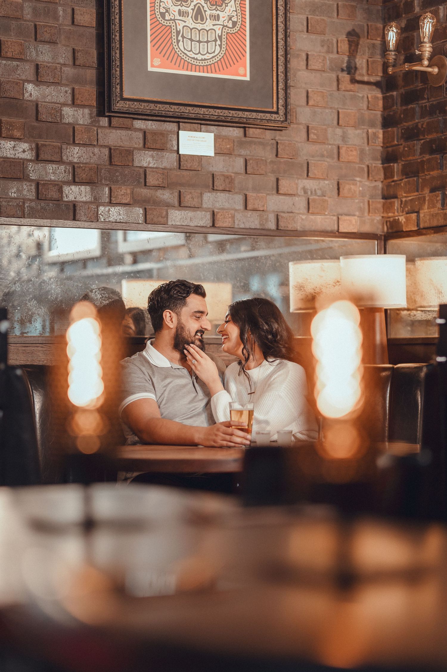 Romantic couple sharing intimate moment in dimly lit restaurant with decorative skull art.