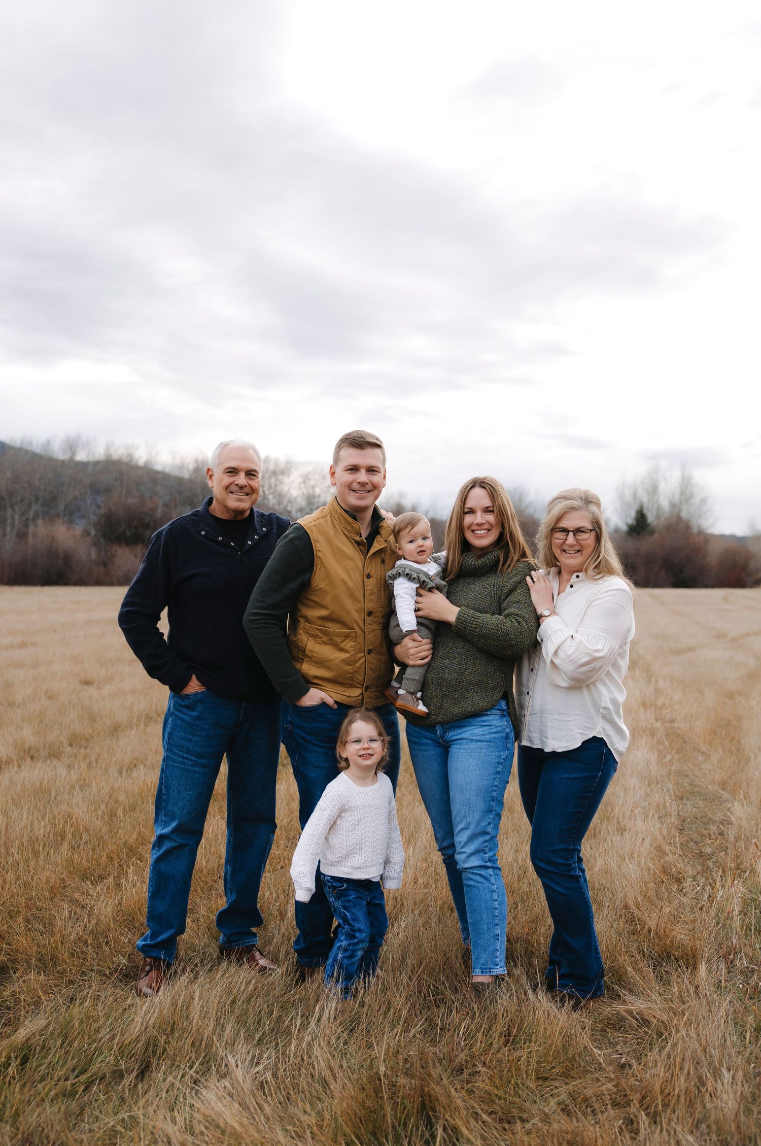 Extended family group portrait in casual attire standing in tall grass field.
