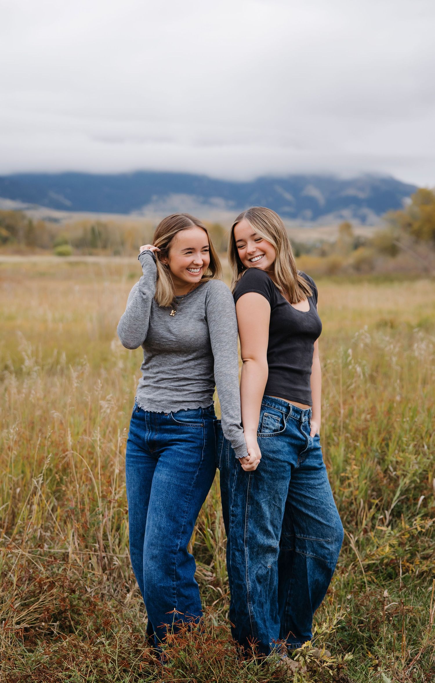 Friends laughing together in a field with mountains visible in the distance.