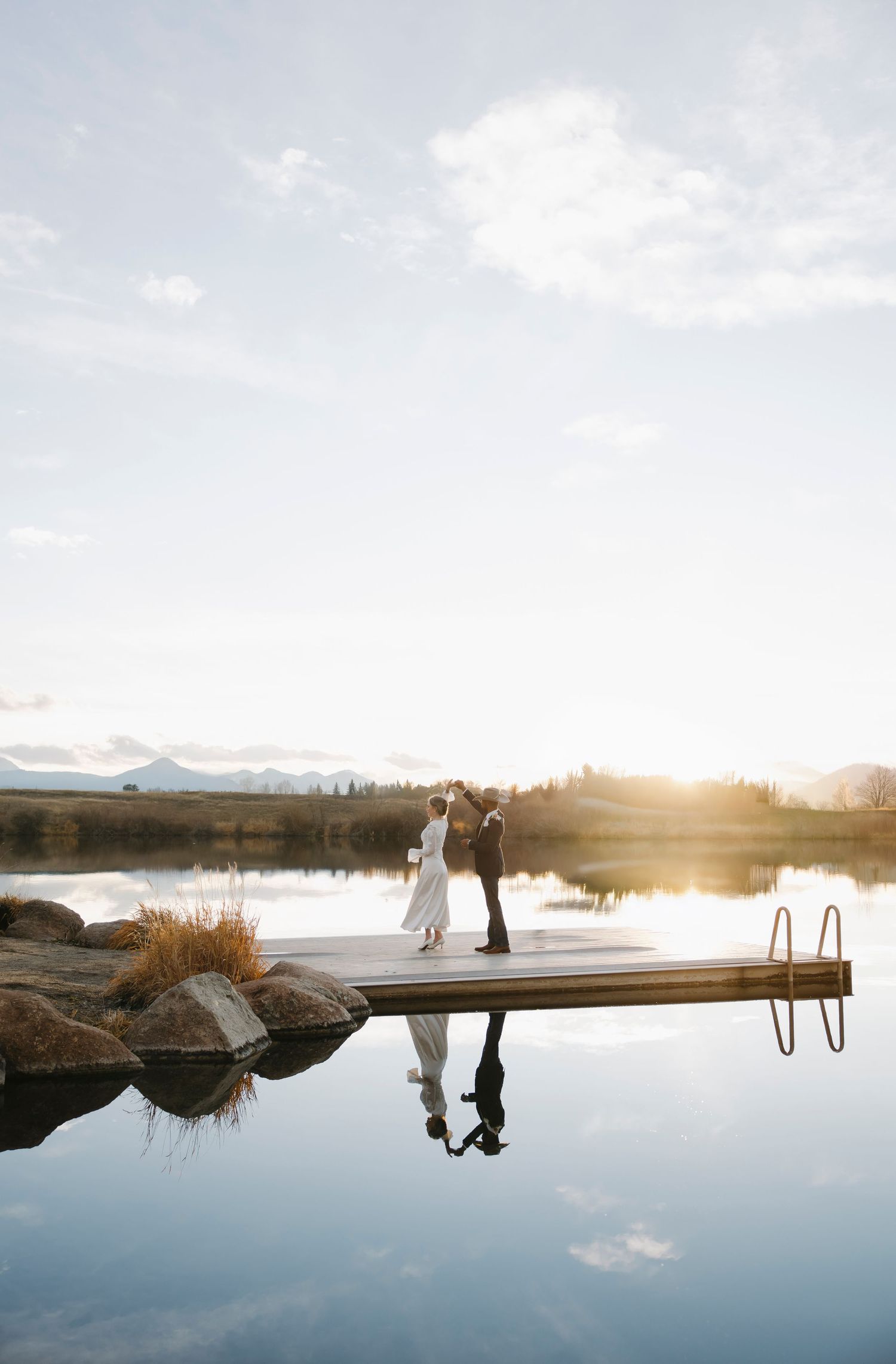 Panoramic landscape wedding photos reflected in still water at sunset with mountains in the background.