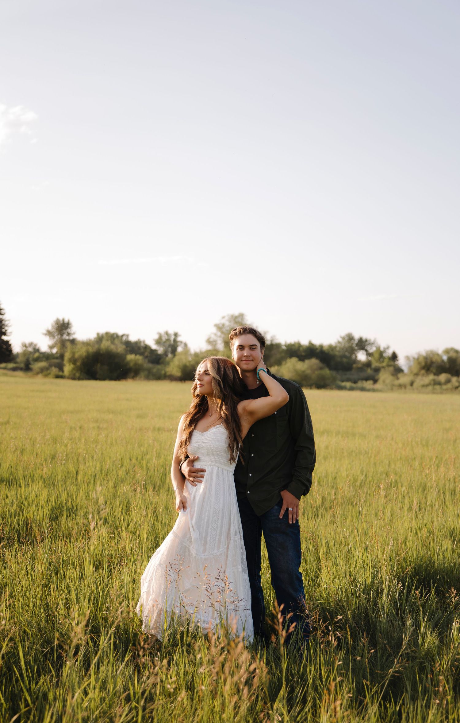 Romantic couple embraces in a sunlit meadow with tall grass during golden hour.