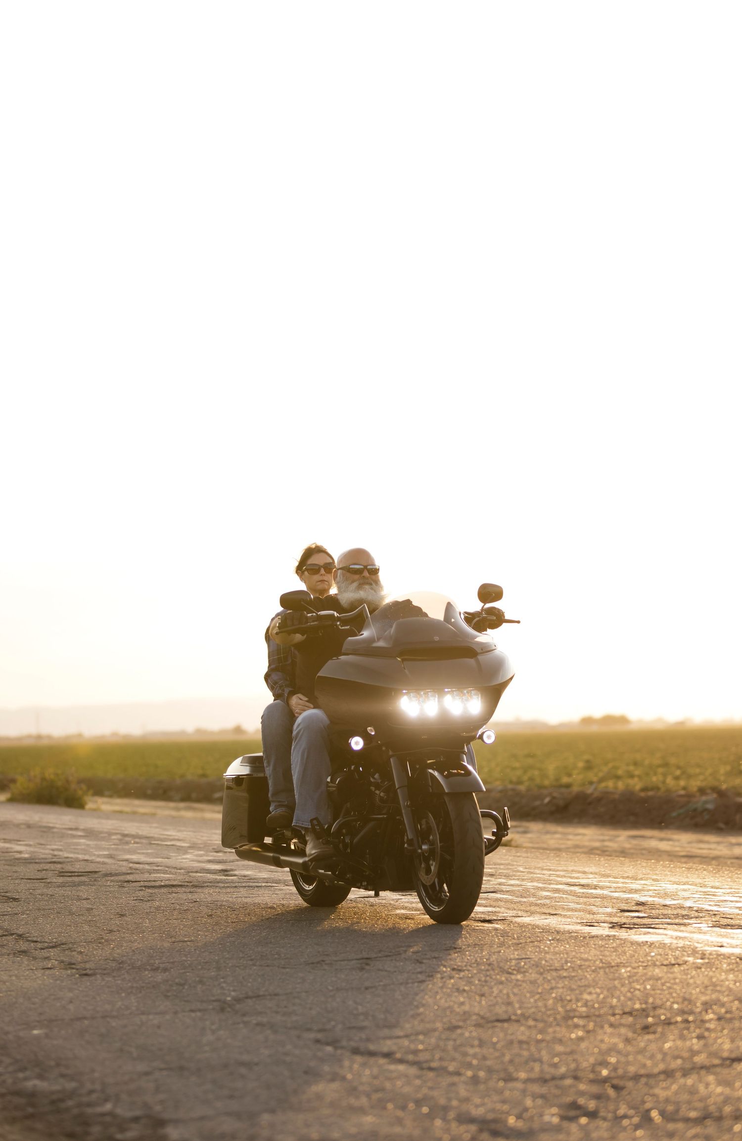 A couple rides a motorcycle together at sunset on an empty road.