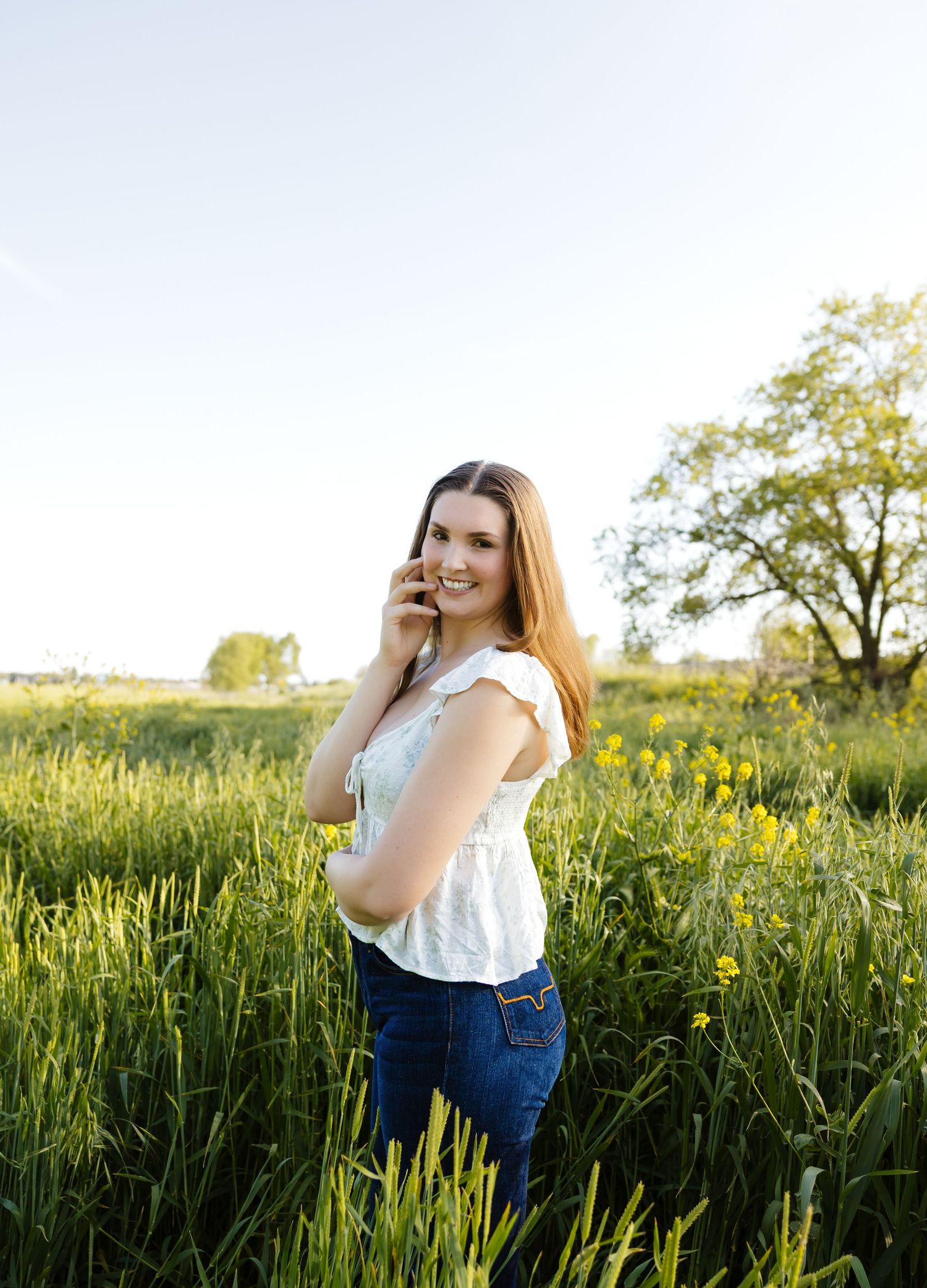 Young woman in white top talking on phone in sunny meadow with wildflowers.
