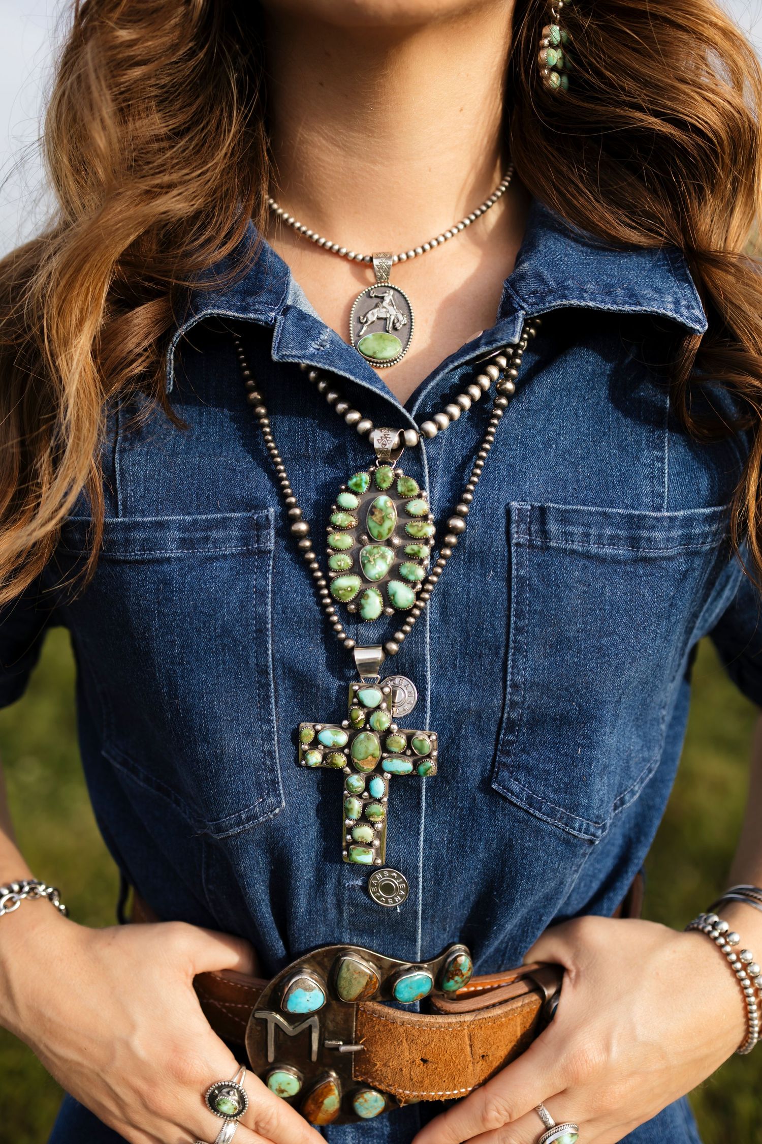 Woman wearing turquoise squash blossom necklaces, silver jewelry, and denim shirt with leather belt.